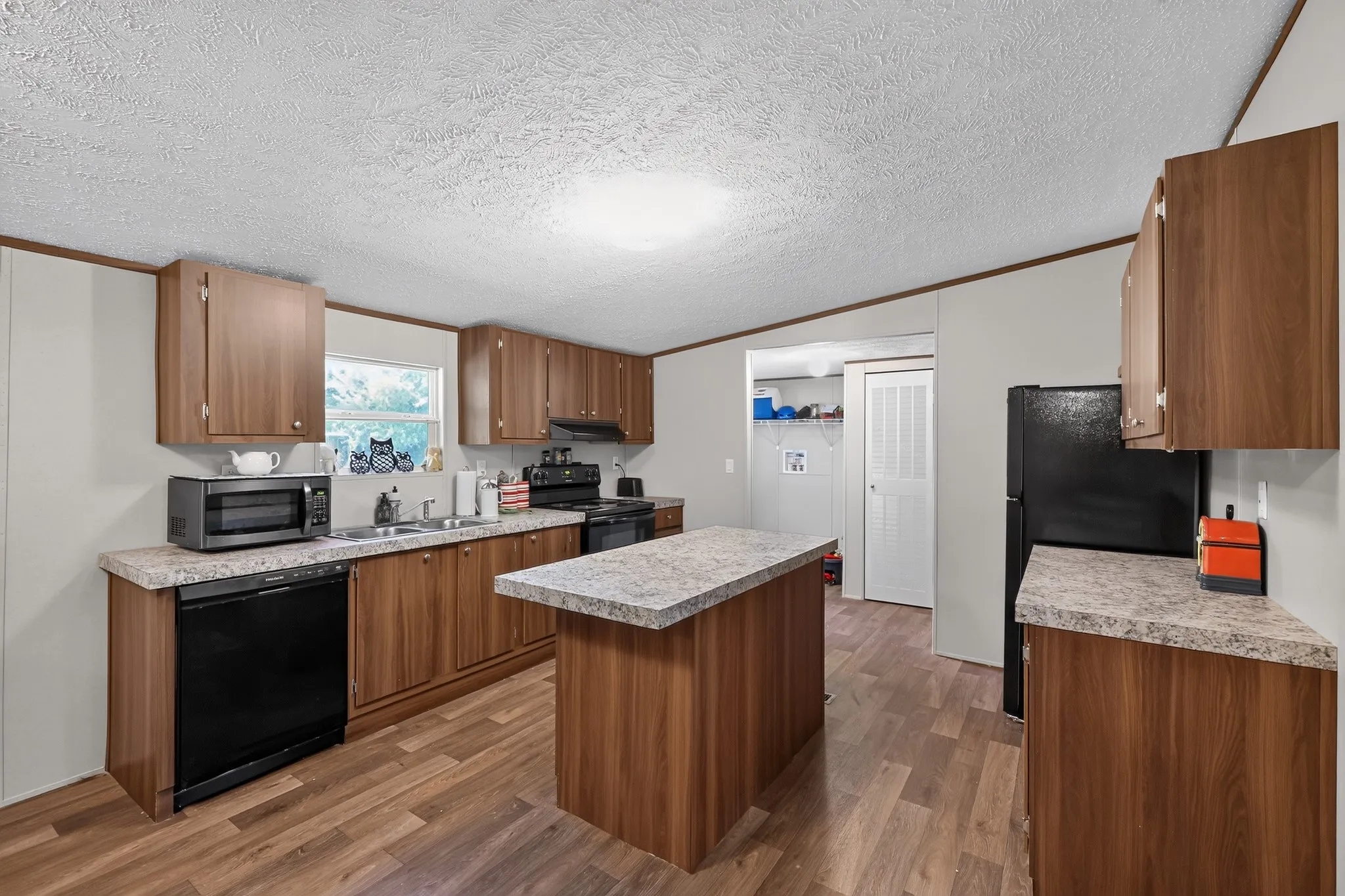 Kitchen featuring wood-finish cabinetry, black appliances, a central island with a countertop, and wood-finish flooring