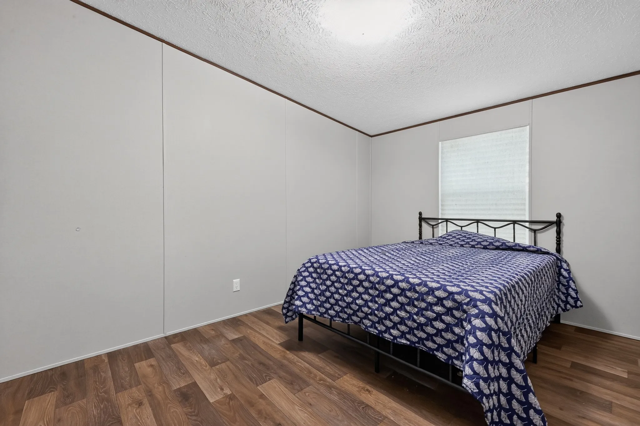 Room featuring wood-finish flooring, light gray walls, a textured white ceiling, a flush-mount ceiling light, and a window with horizontal blinds