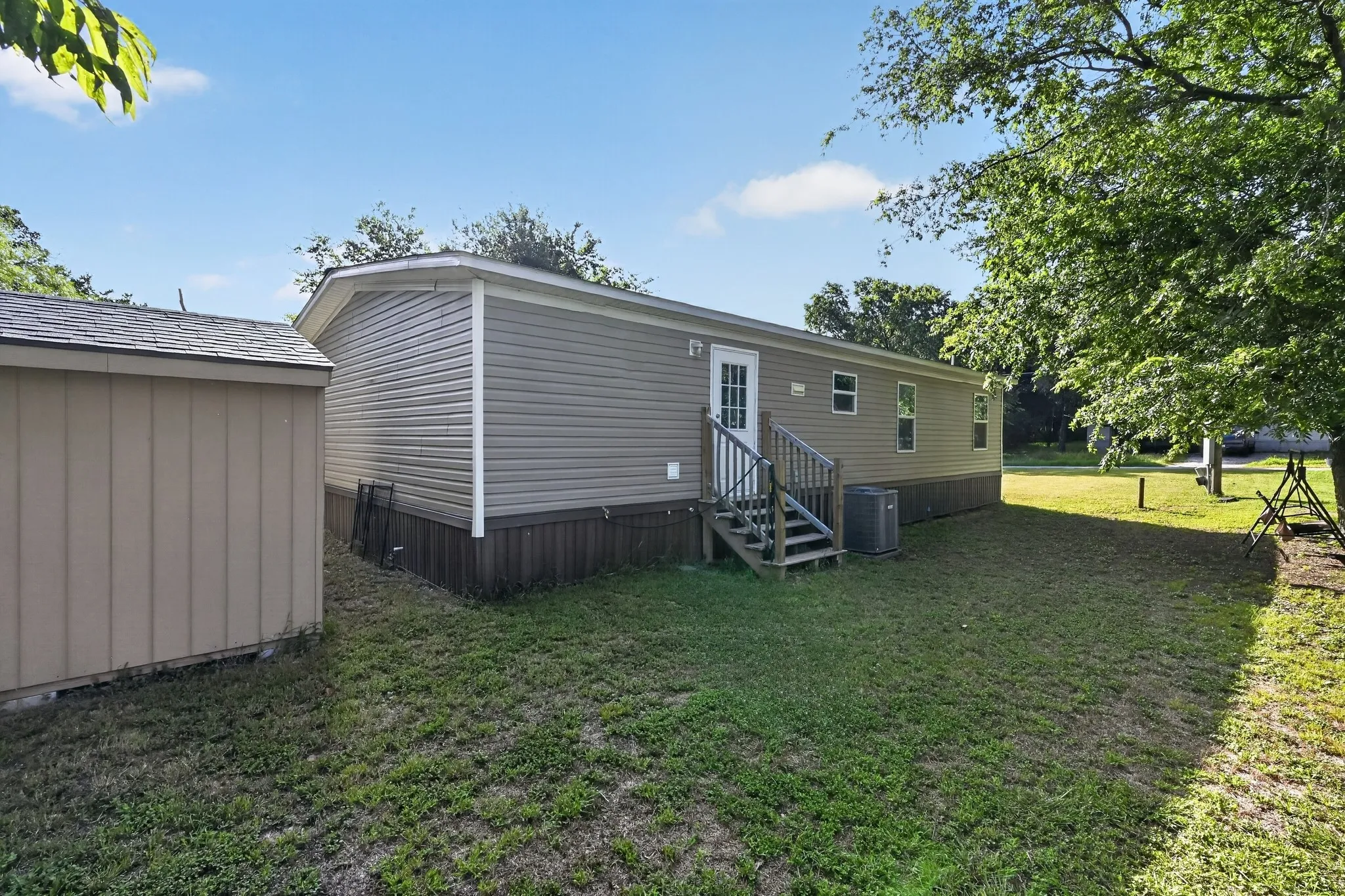 Exterior featuring tan horizontal siding, a white entry door, and a dedicated storage shed