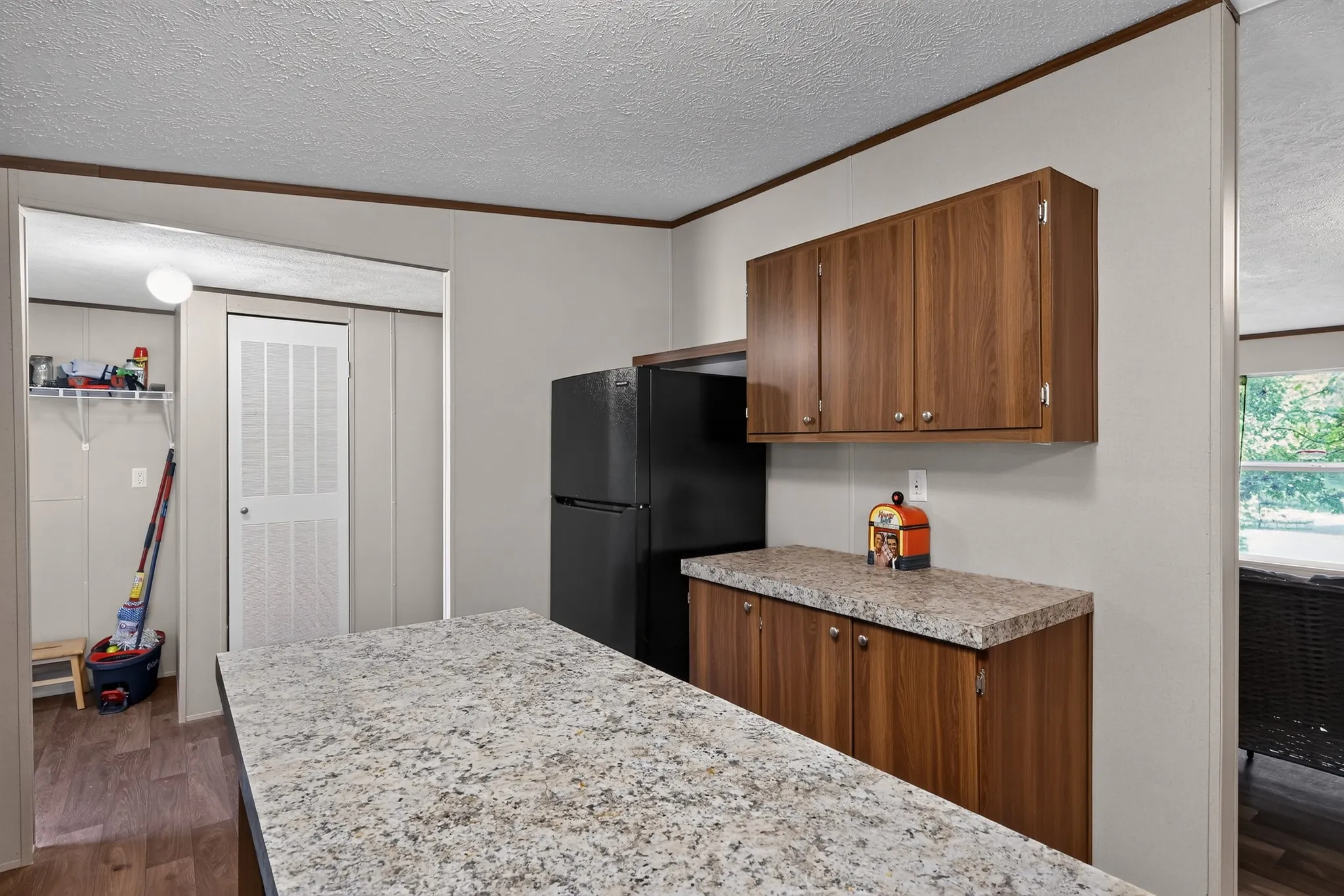 Kitchen featuring wood-finish cabinetry, speckled countertops, a black refrigerator, and wood-finish flooring