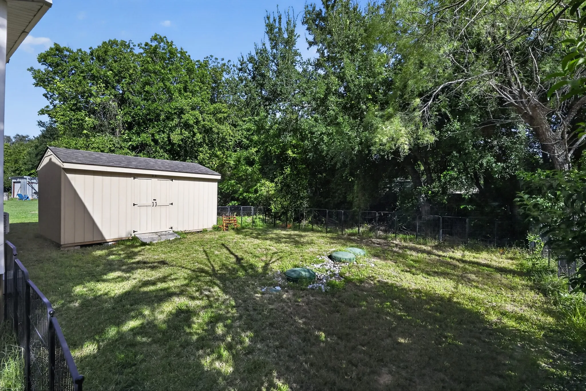 Expansive backyard featuring a large storage shed with double doors, mature perimeter trees, and a black metal fence line