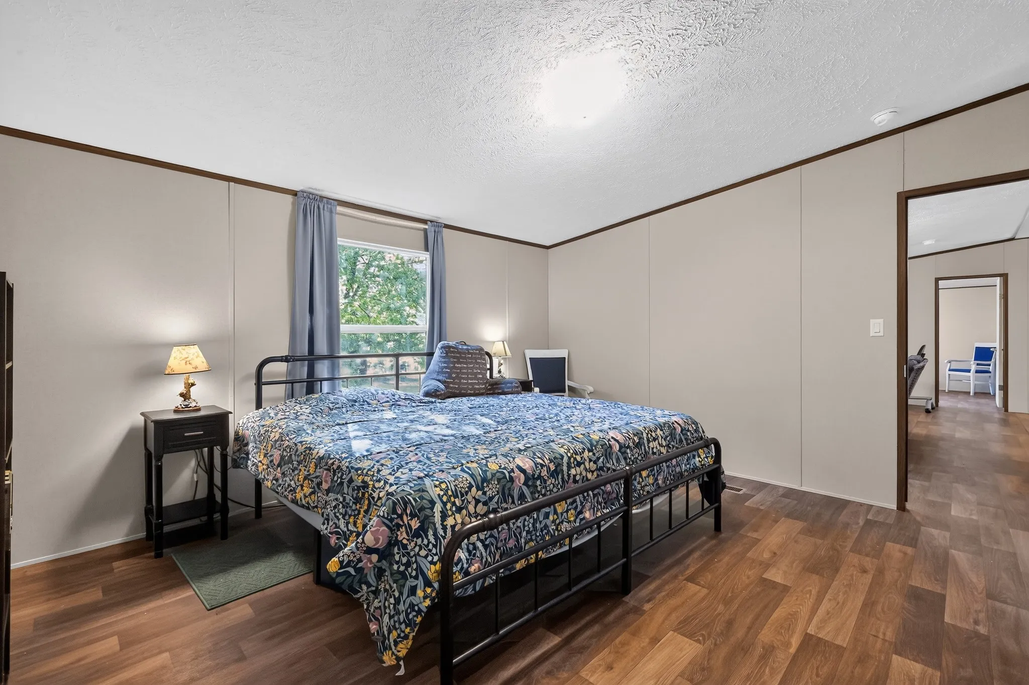 Bedroom featuring wood-finish flooring, neutral wall paneling, and a window with natural light
