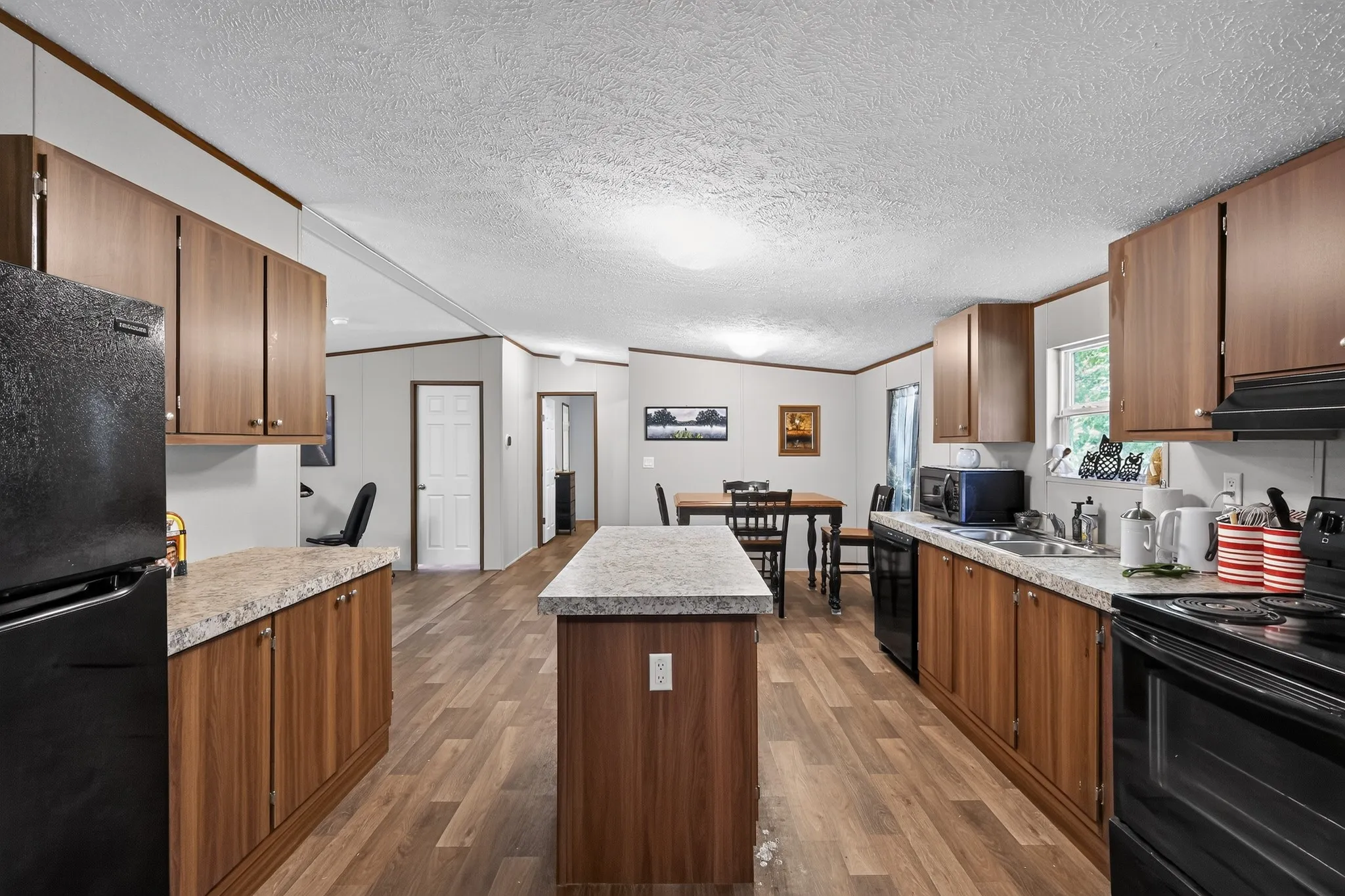 Open-concept kitchen featuring wood-finish flooring, wood cabinetry, stone-look countertops, and a central island