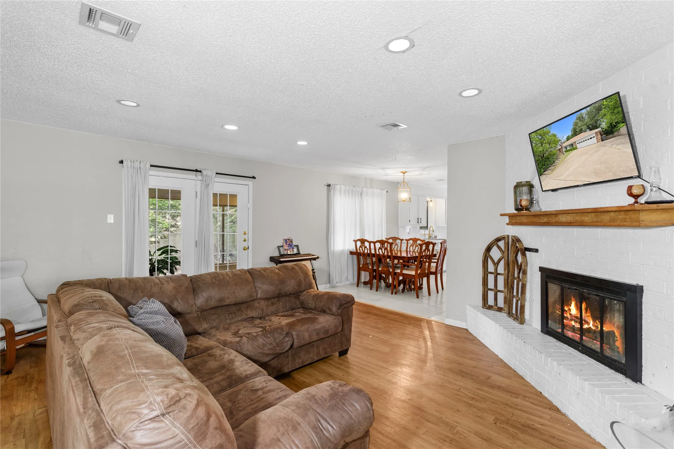 Living area featuring a white brick fireplace with a wood mantel, wood-finish flooring, recessed lighting, and French doors