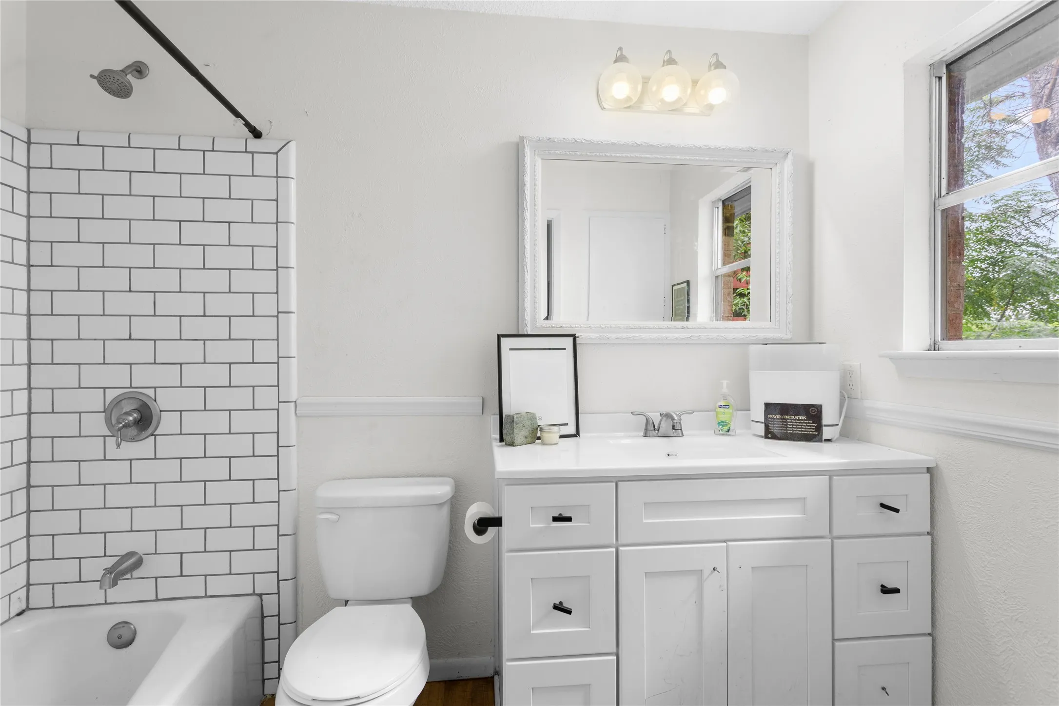 Bathroom featuring a white subway tile shower, white vanity with integrated sink, white cabinetry with black hardware, and an ornate framed mirror