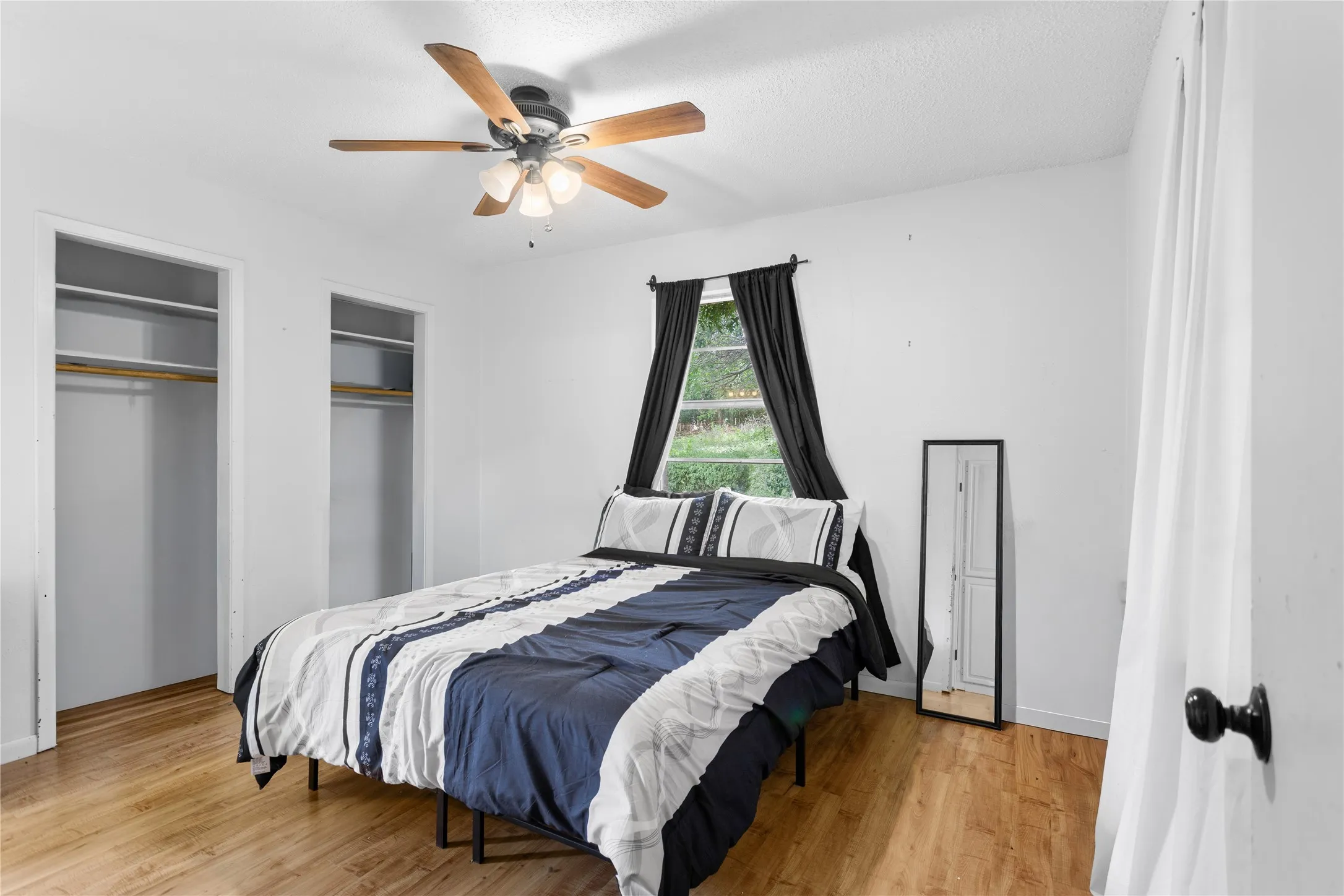 Bedroom featuring wood-finish flooring, a ceiling fan with integrated lighting, and a window with dark curtains