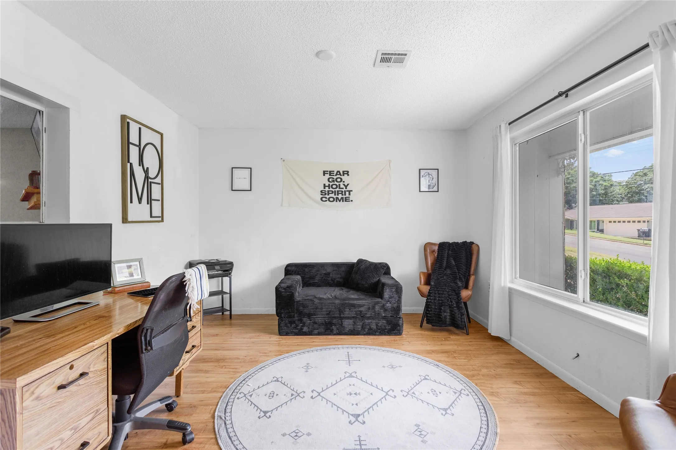 Bright interior room featuring a large window, light wood-finish flooring, white walls, and a recessed ceiling light