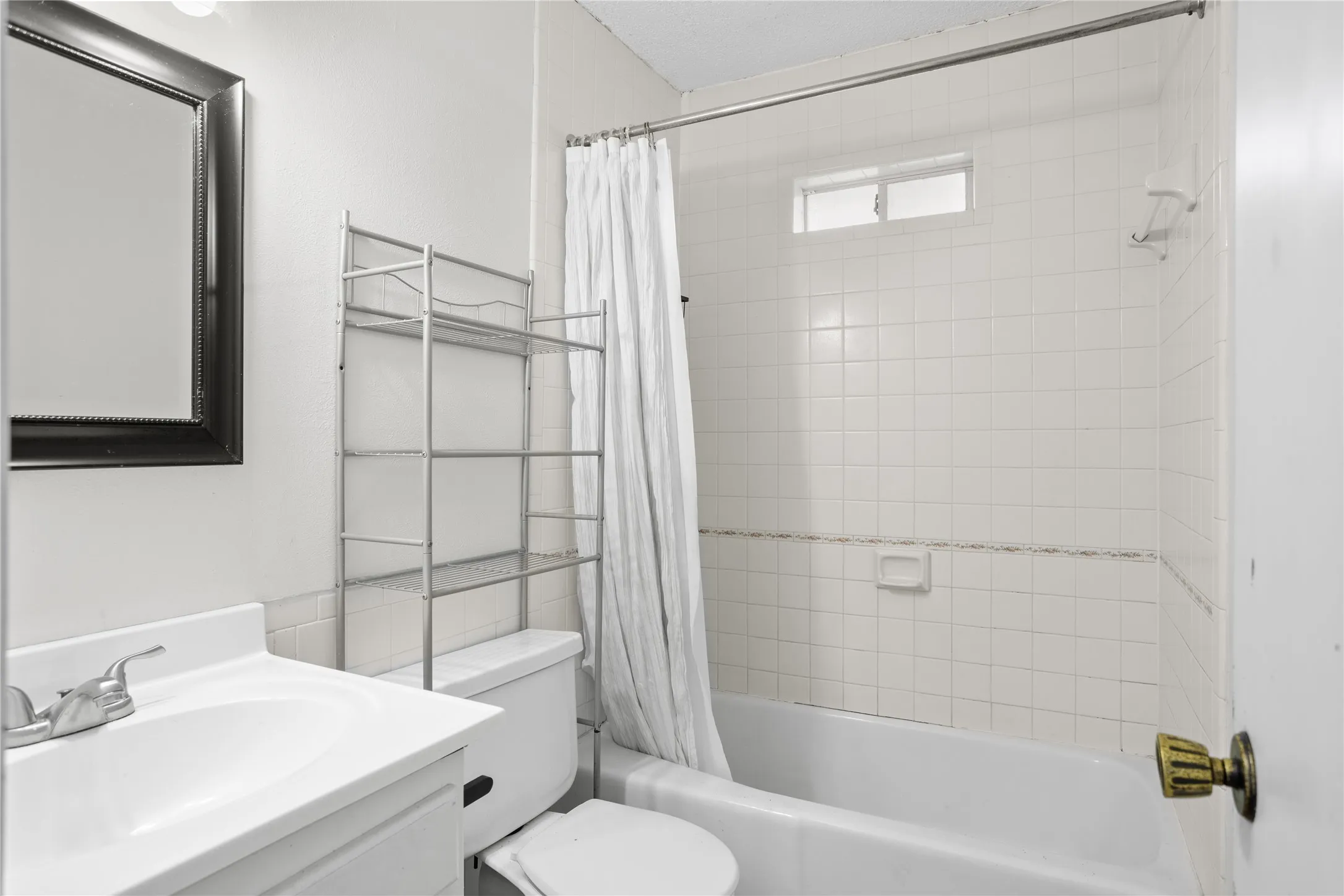 White bathroom featuring a bathtub with a tiled surround, a small window, a vanity with an integrated sink, and a framed mirror