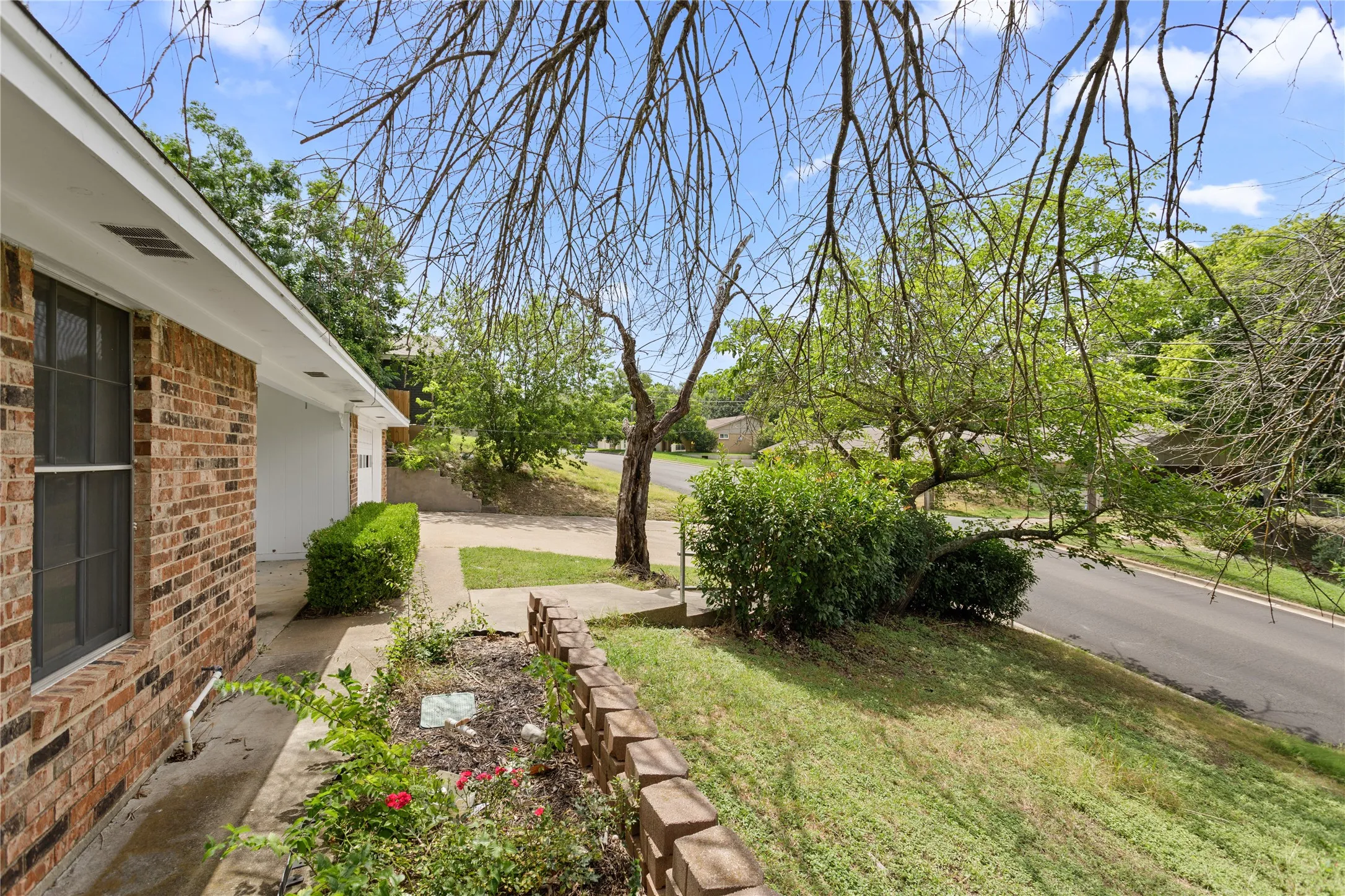 Brick exterior with white soffit, mature landscaping, concrete walkway, and a driveway