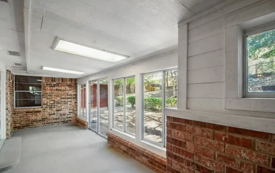 Sunroom featuring a full wall of windows, exposed brick accents, fluorescent overhead lighting, and concrete flooring
