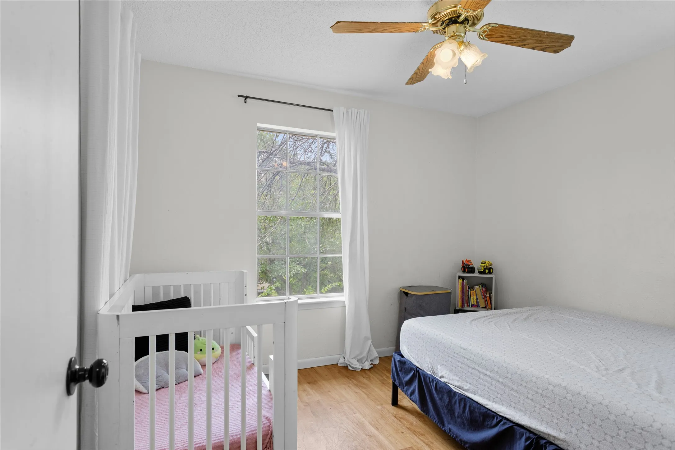 Bedroom featuring a ceiling fan with integrated lighting, wood-finish flooring, and a window with white drapes