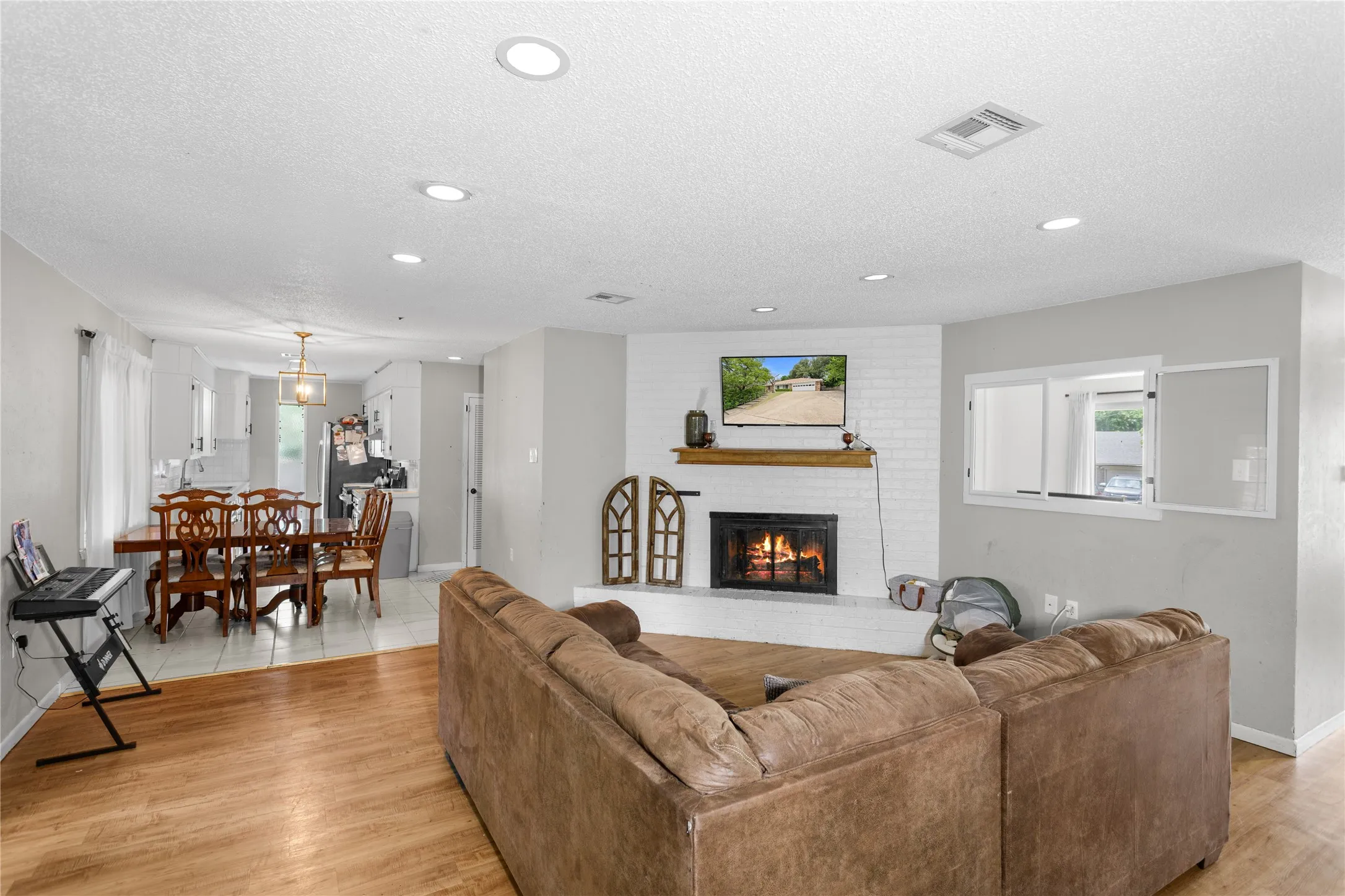 Living area featuring a white brick fireplace with a wood mantle, wood-finish flooring, recessed lighting, and a pass-through window