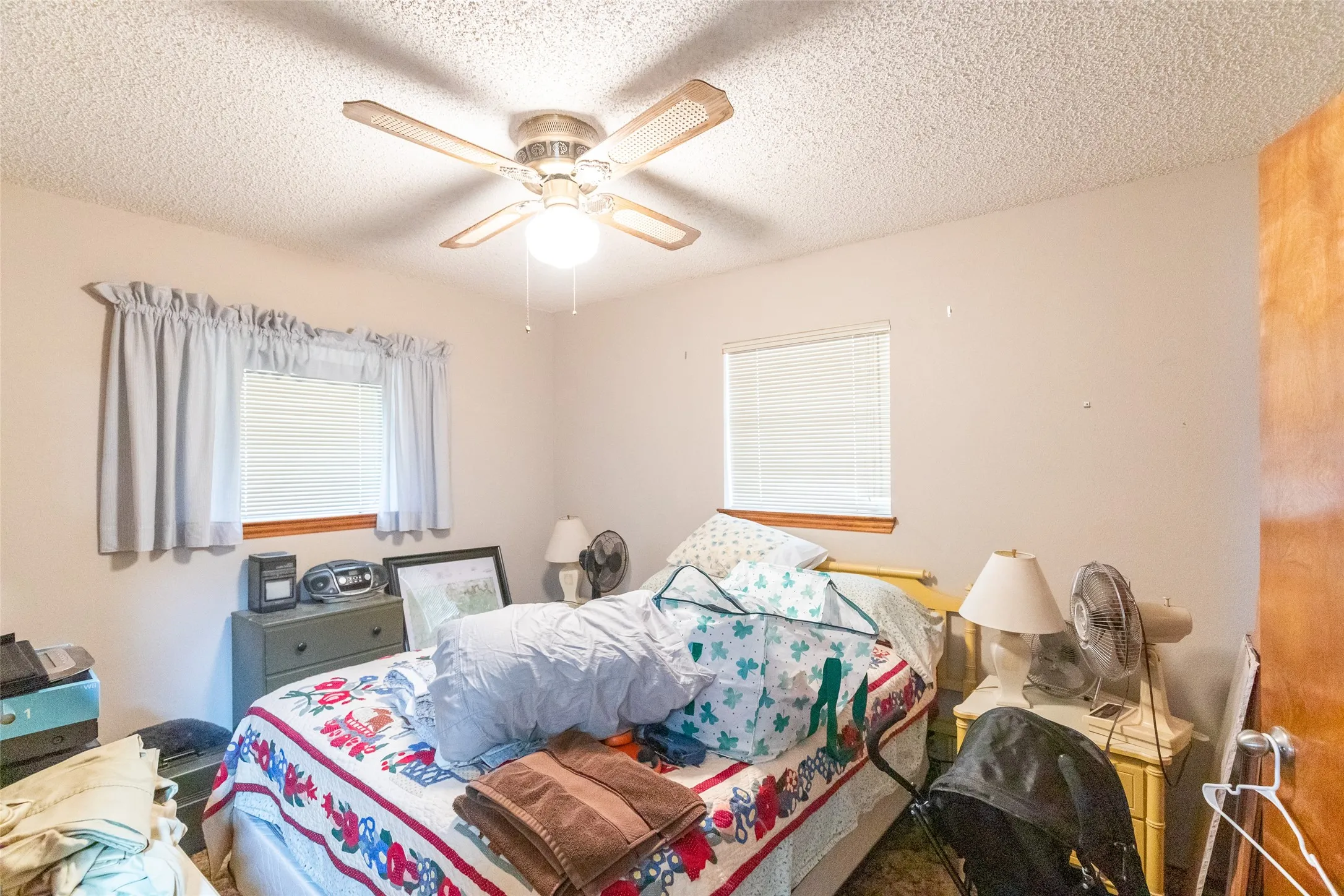 Bedroom featuring a ceiling fan with integrated lighting, two windows with blinds and valances, and wood trim