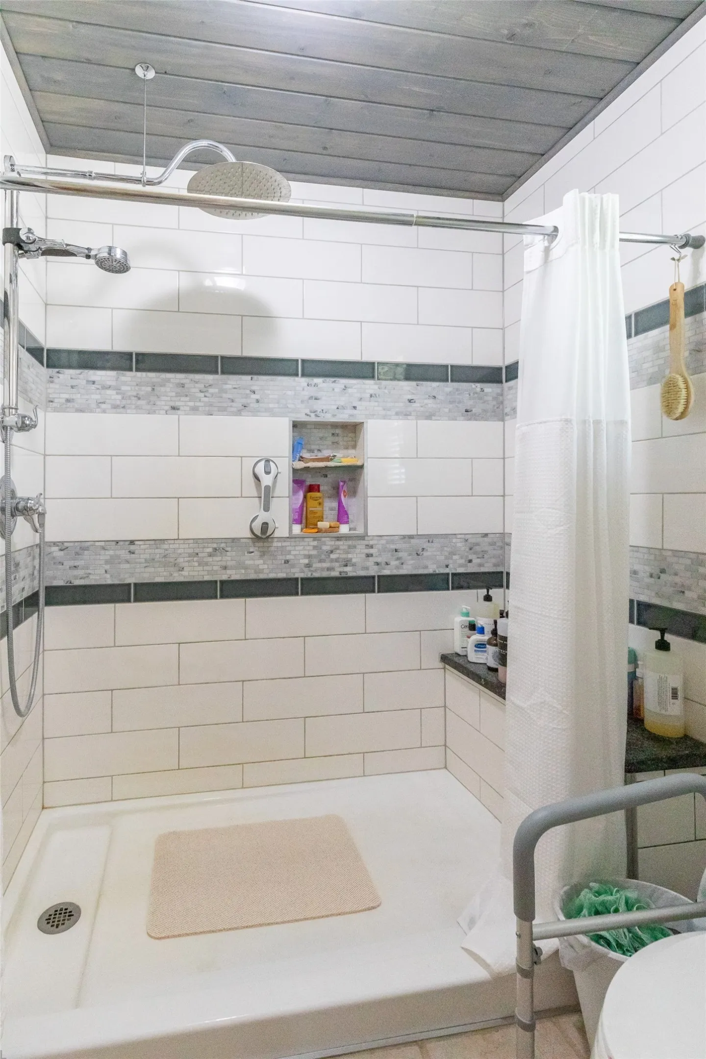 Walk-in shower featuring white subway tile, decorative accent bands, a built-in shower niche, a rain shower head, and a wood-finish ceiling