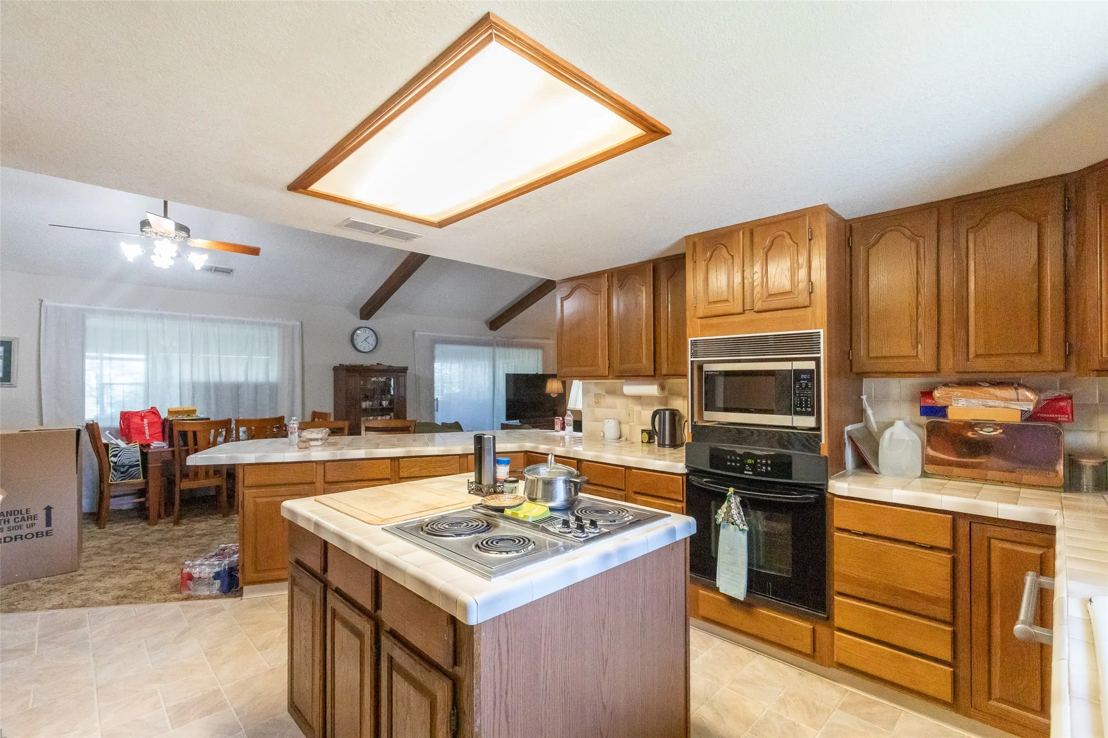 Kitchen featuring wood-finish cabinetry, built-in black appliances, and a central island with an integrated cooktop