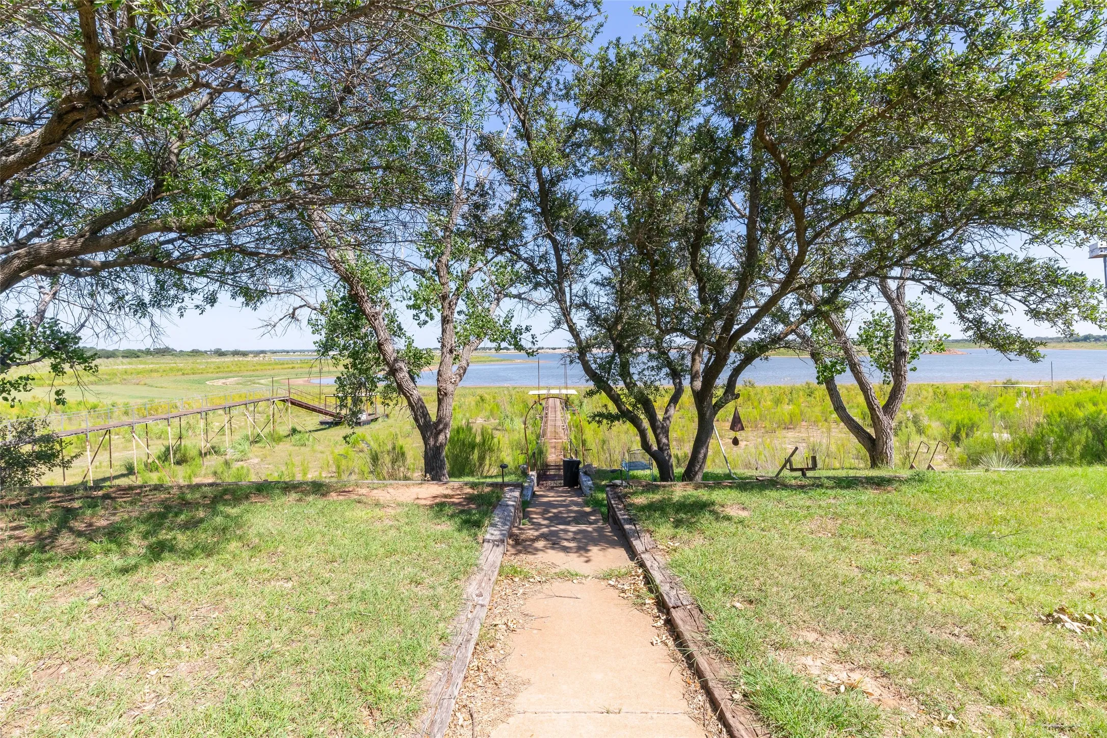 Lakeside property featuring mature trees and a wooden walkway extending to the water