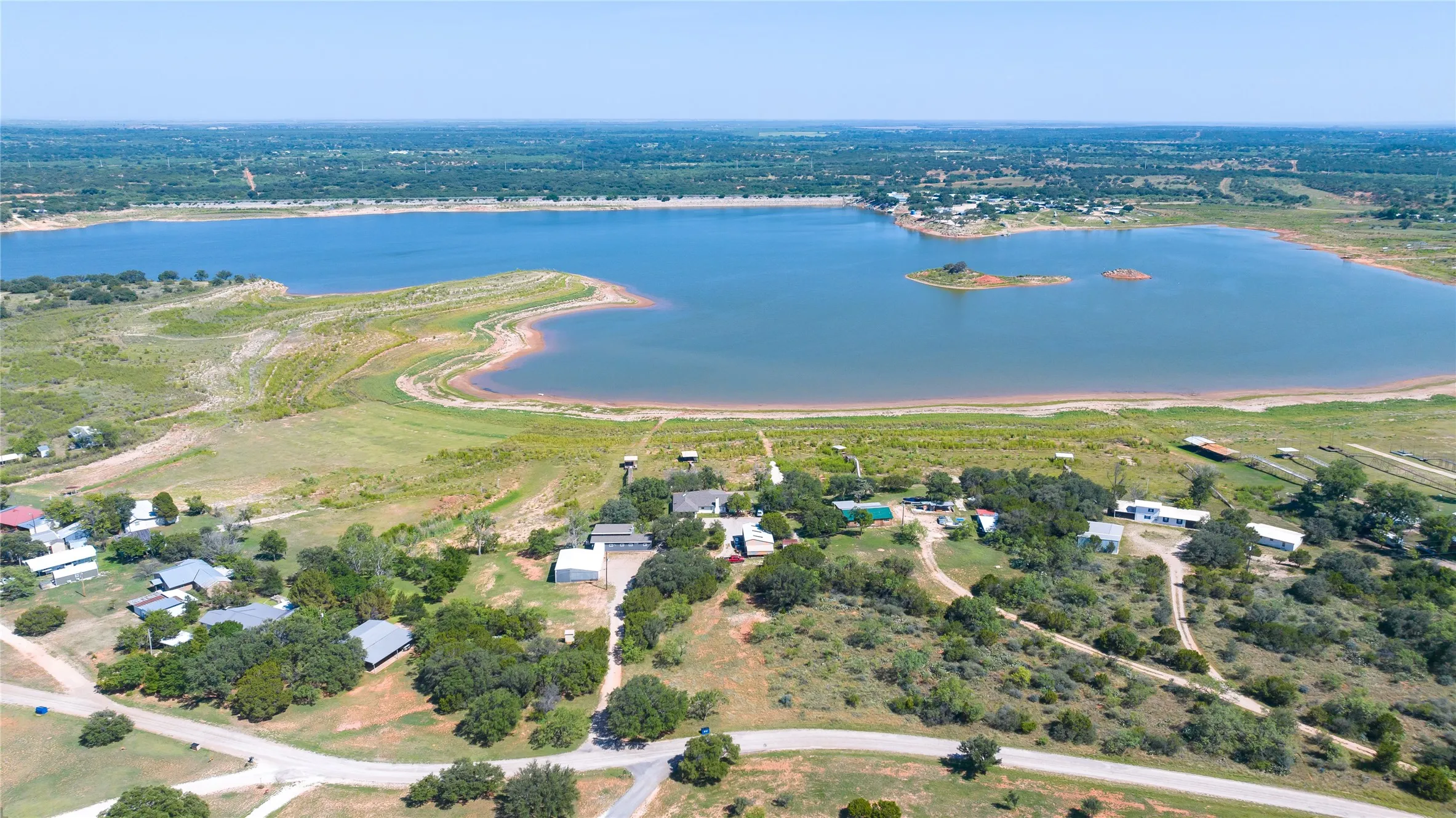 Expansive lakefront property featuring a broad body of water, a verdant shoreline, and multiple structures