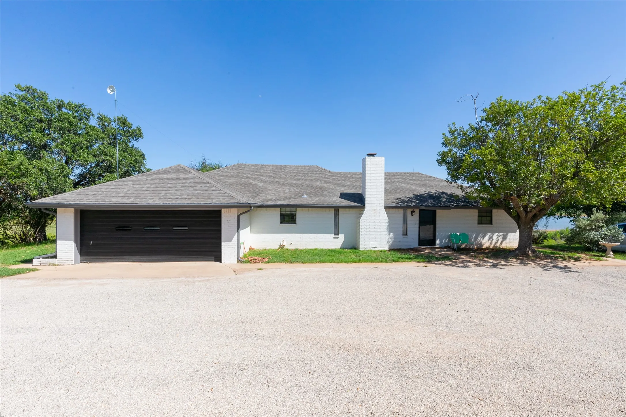 Single-story residence featuring a two-car garage with a dark door, a white brick exterior, and a grey shingle roof