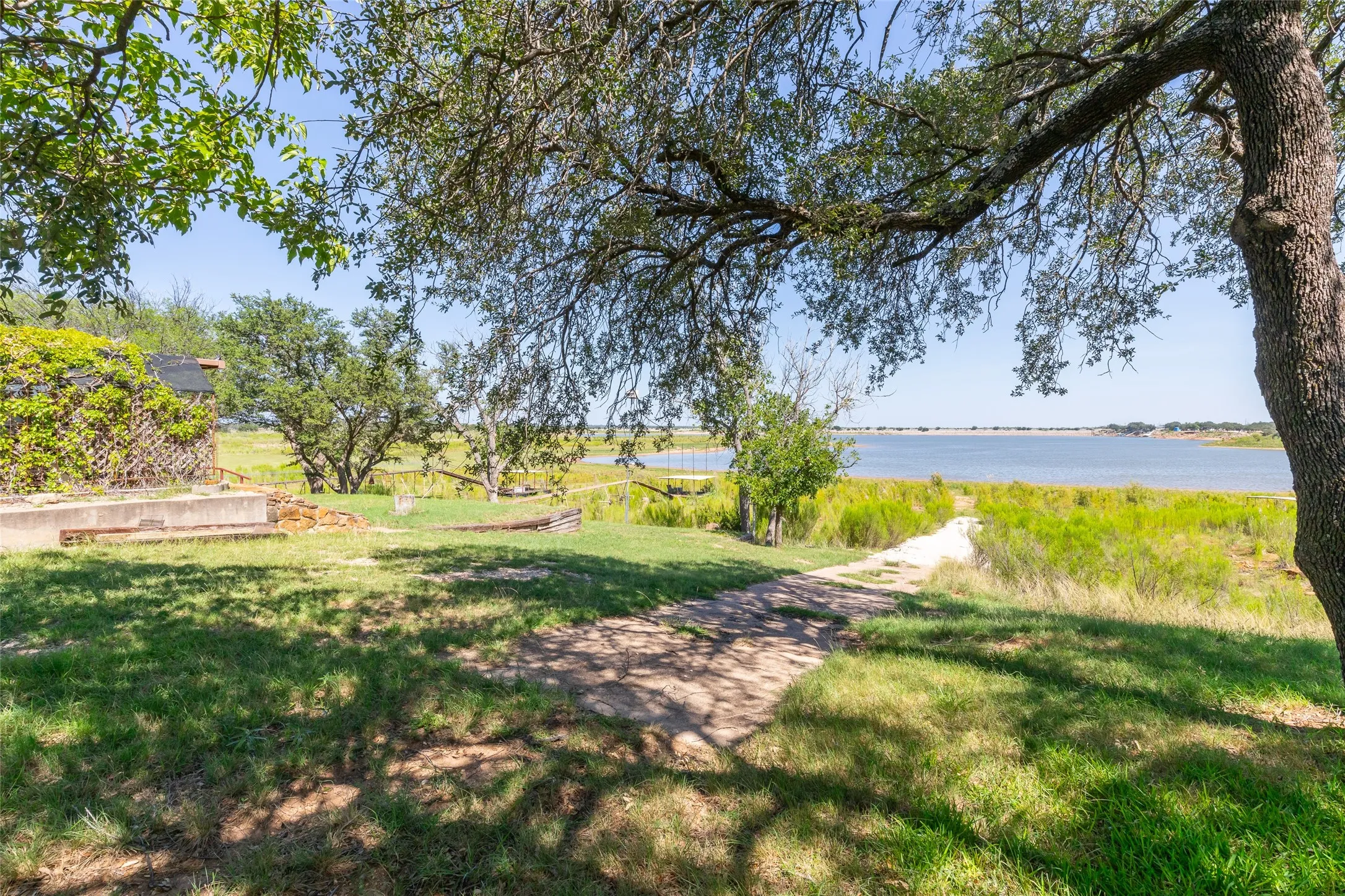 Expansive green space with mature trees providing partial shade, and a pathway leading to the water's edge