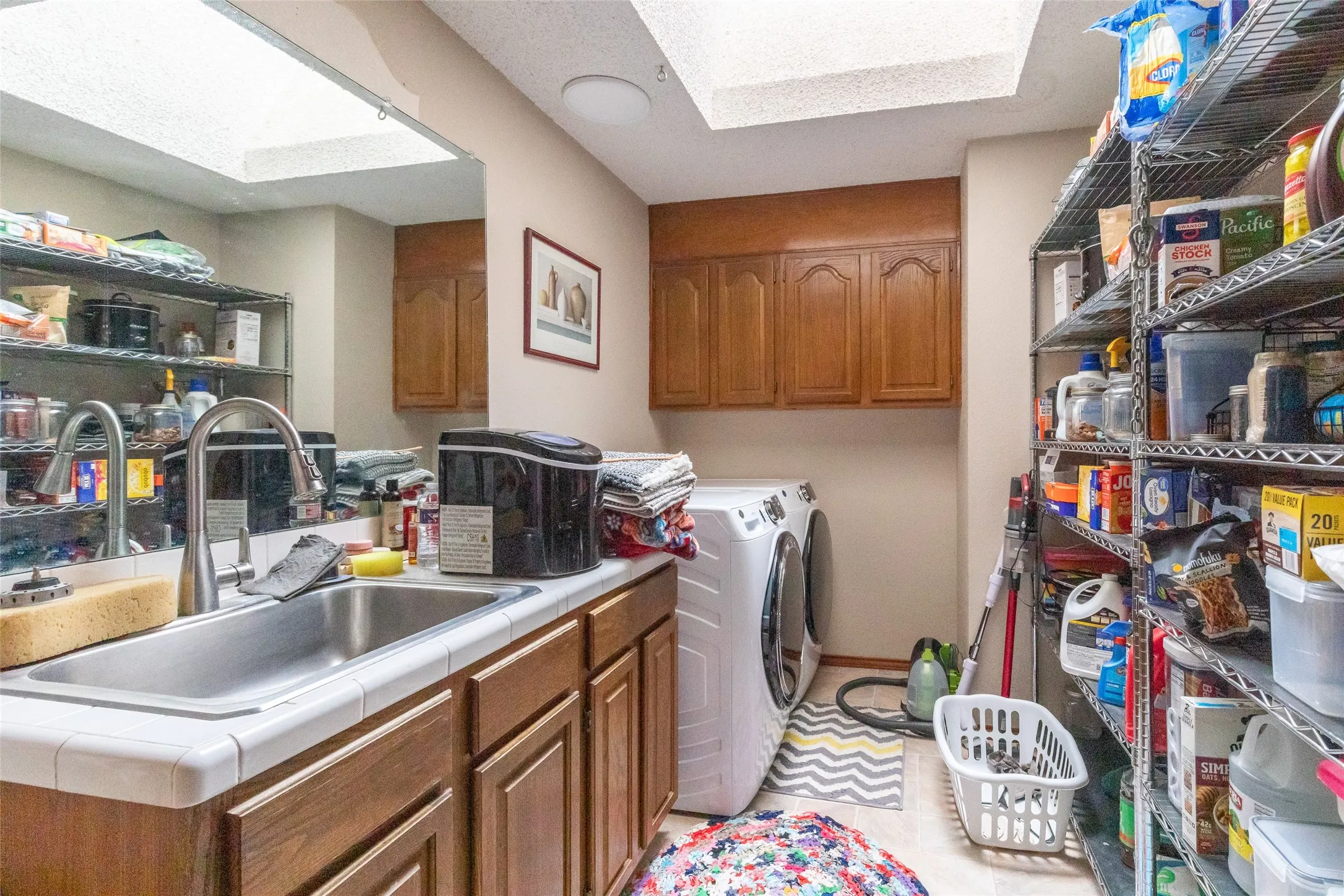 Utility room with a stainless steel sink, wood-finish cabinetry, and overhead skylights