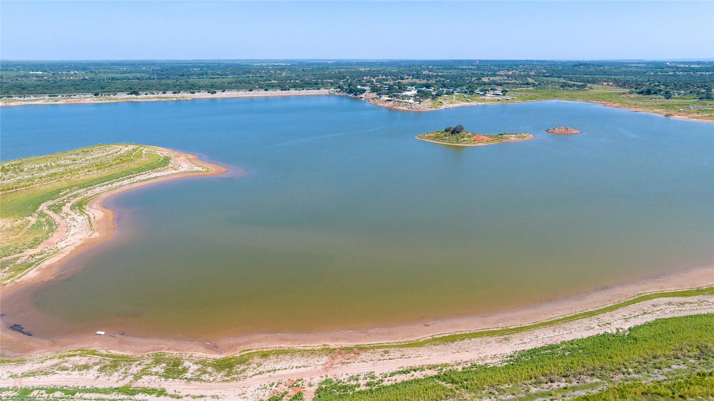 Expansive lake with a broad shoreline, featuring distant green islands and a tree-lined horizon