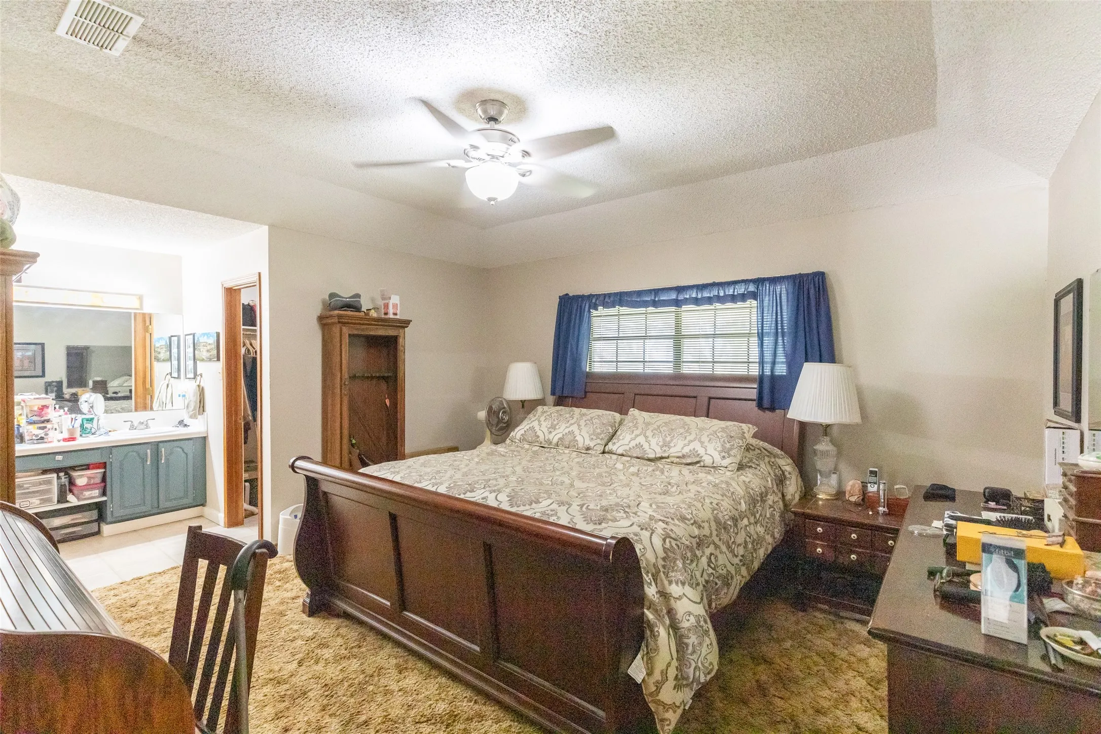 Spacious bedroom featuring textured carpeting, a ceiling fan with integrated lighting, and a window with natural light