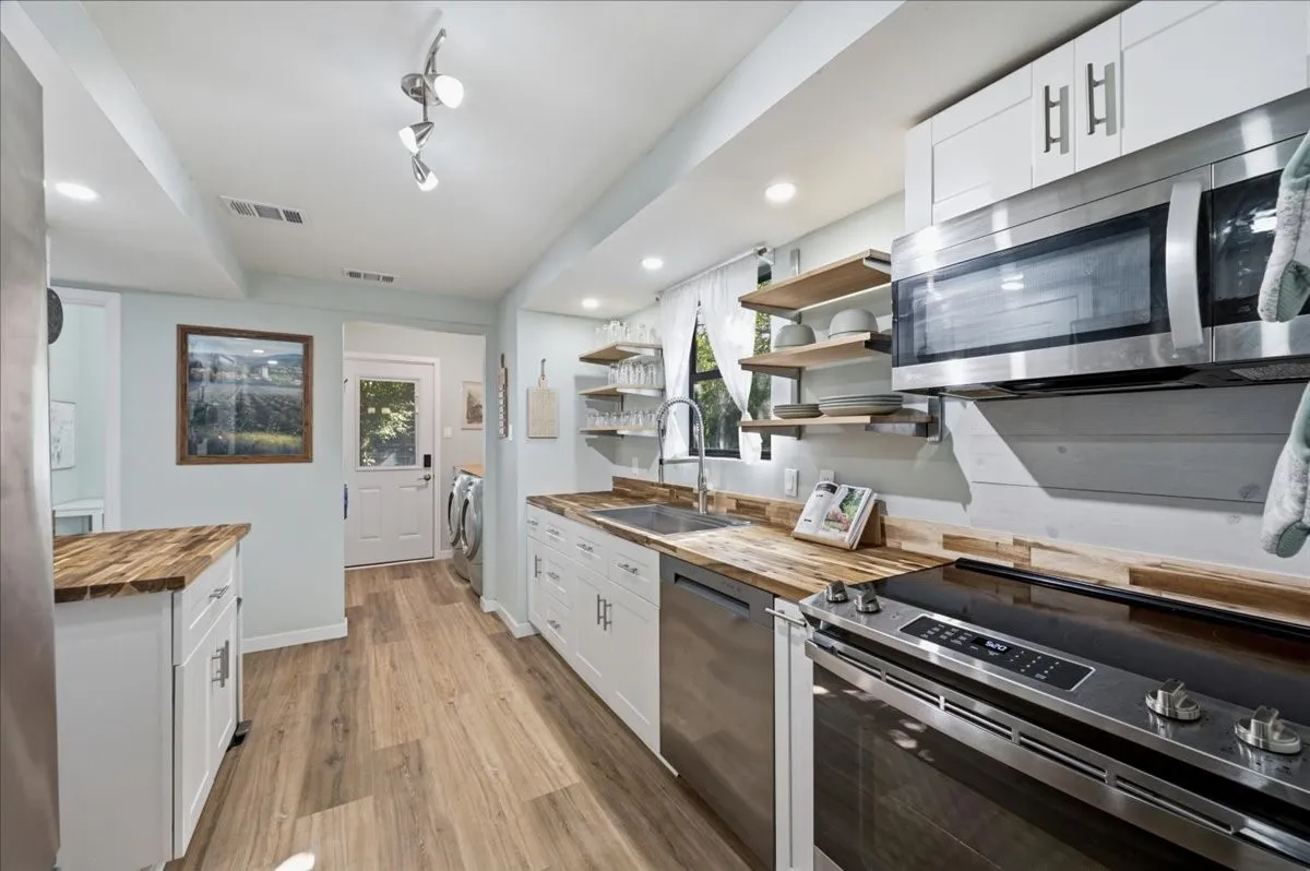 Contemporary kitchen featuring wood-finish flooring, white cabinetry, integrated stainless steel appliances, butcher block countertops, and open shelving
