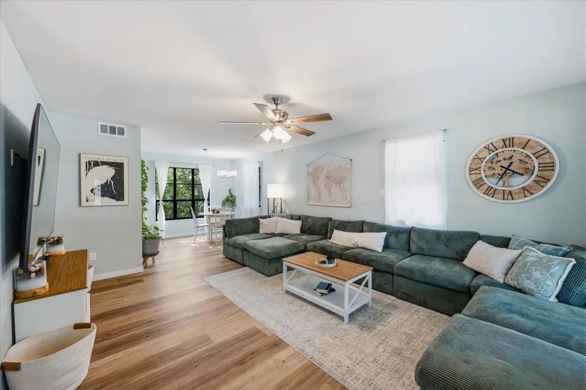 Open-concept living area featuring wood-finish flooring, light-toned walls, and a ceiling fan with integrated lighting