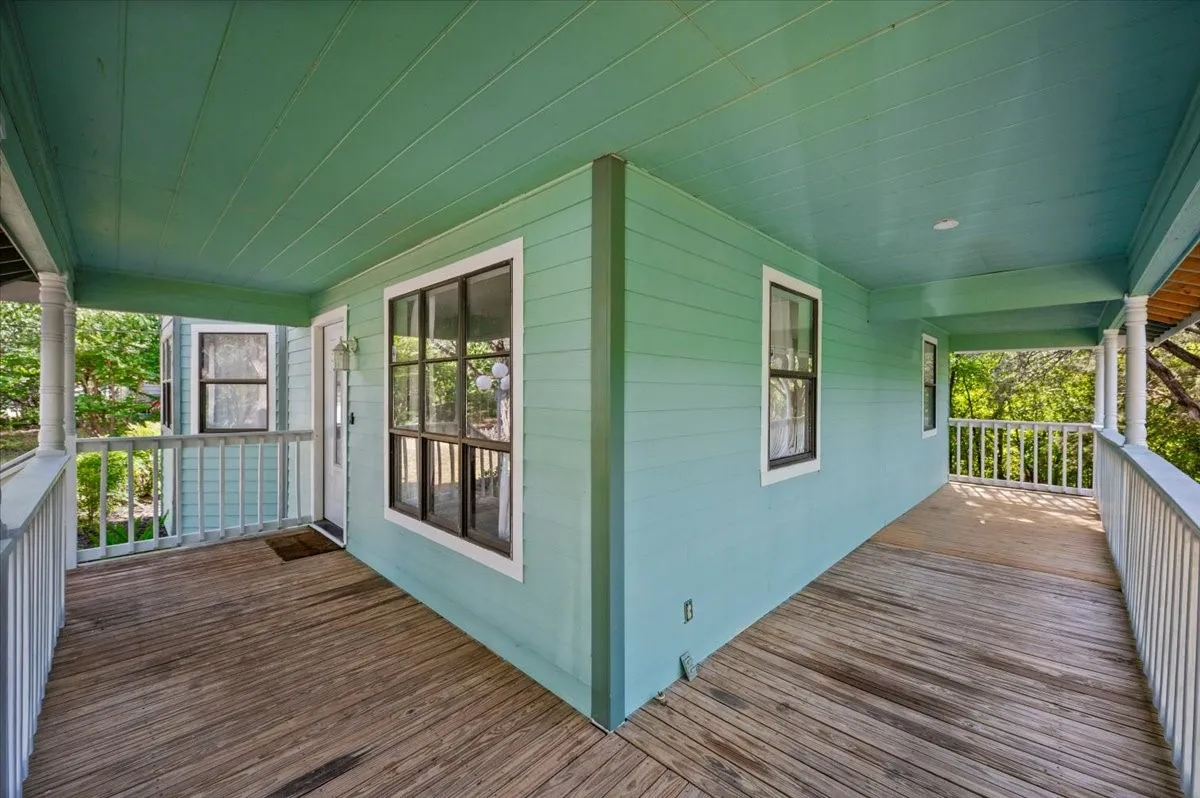 Expansive wrap-around porch featuring wood plank flooring, white spindle railings, and a soft blue-green exterior siding