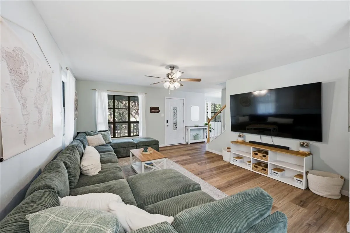 Spacious living area featuring wood-finish flooring, a ceiling fan with light fixture, and multiple windows providing natural light