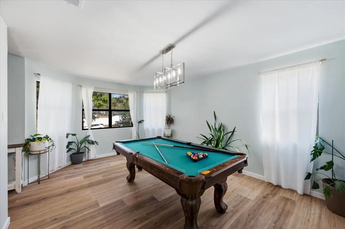 Spacious recreation room featuring wood-finish flooring, multiple windows, and a contemporary chandelier