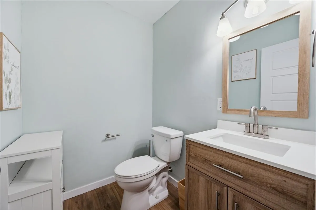 Powder room featuring wood-finish flooring, a white toilet, and a vanity with a white countertop and wood-finish cabinetry