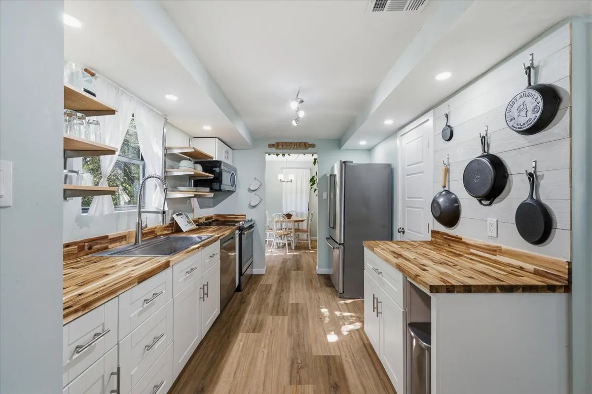 Bright kitchen featuring wood-finish flooring, white cabinetry with silver hardware, butcher block countertops, a stainless steel sink, and stainless steel appliances