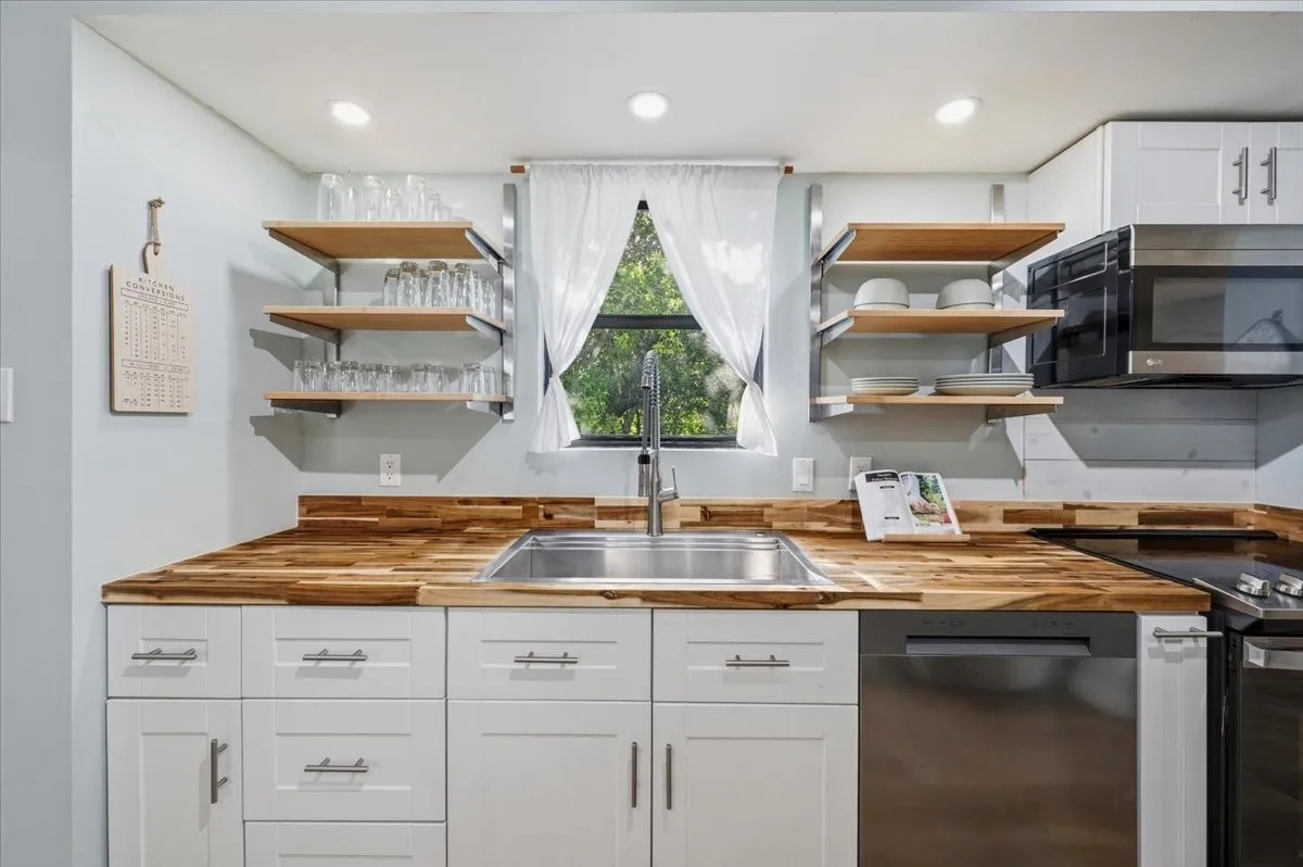 Kitchen featuring white cabinetry with brushed nickel hardware, wood-finish countertops, stainless steel sink, and open shelving