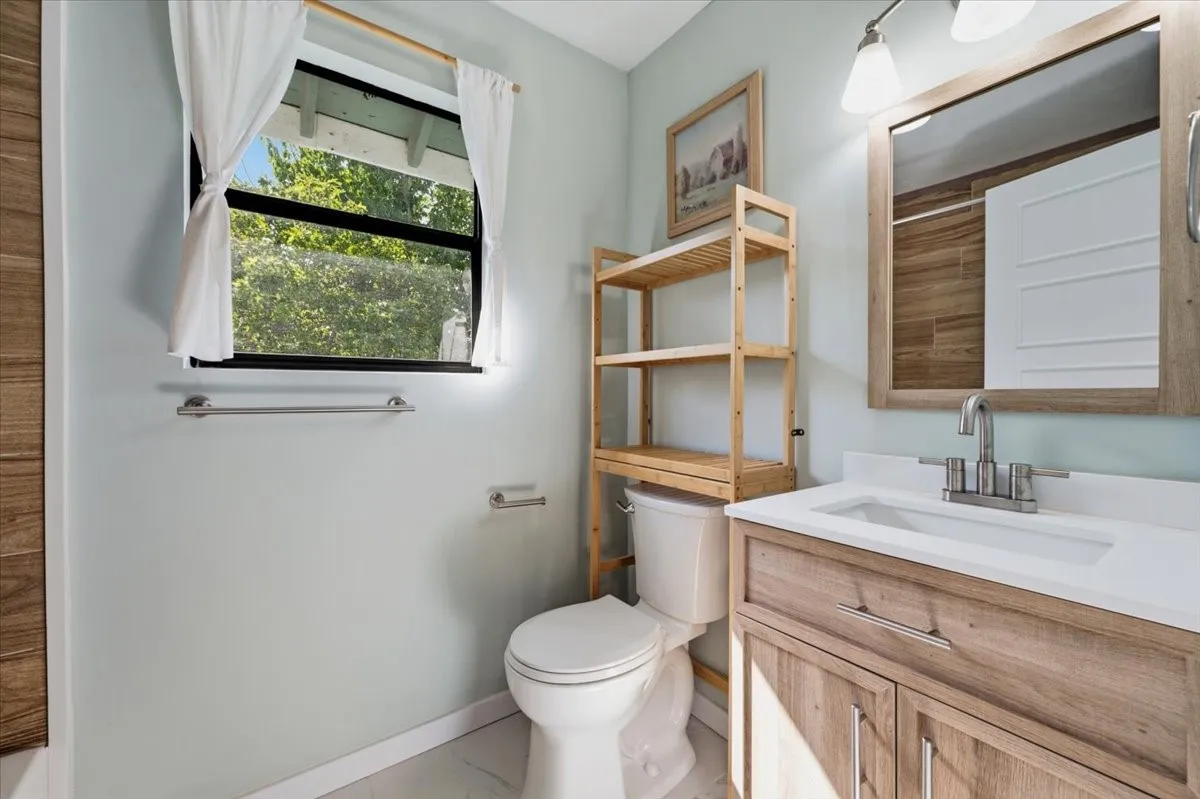 Bathroom featuring a wood-finish vanity with an integrated sink, a rectangular mirror, and a window providing natural illumination