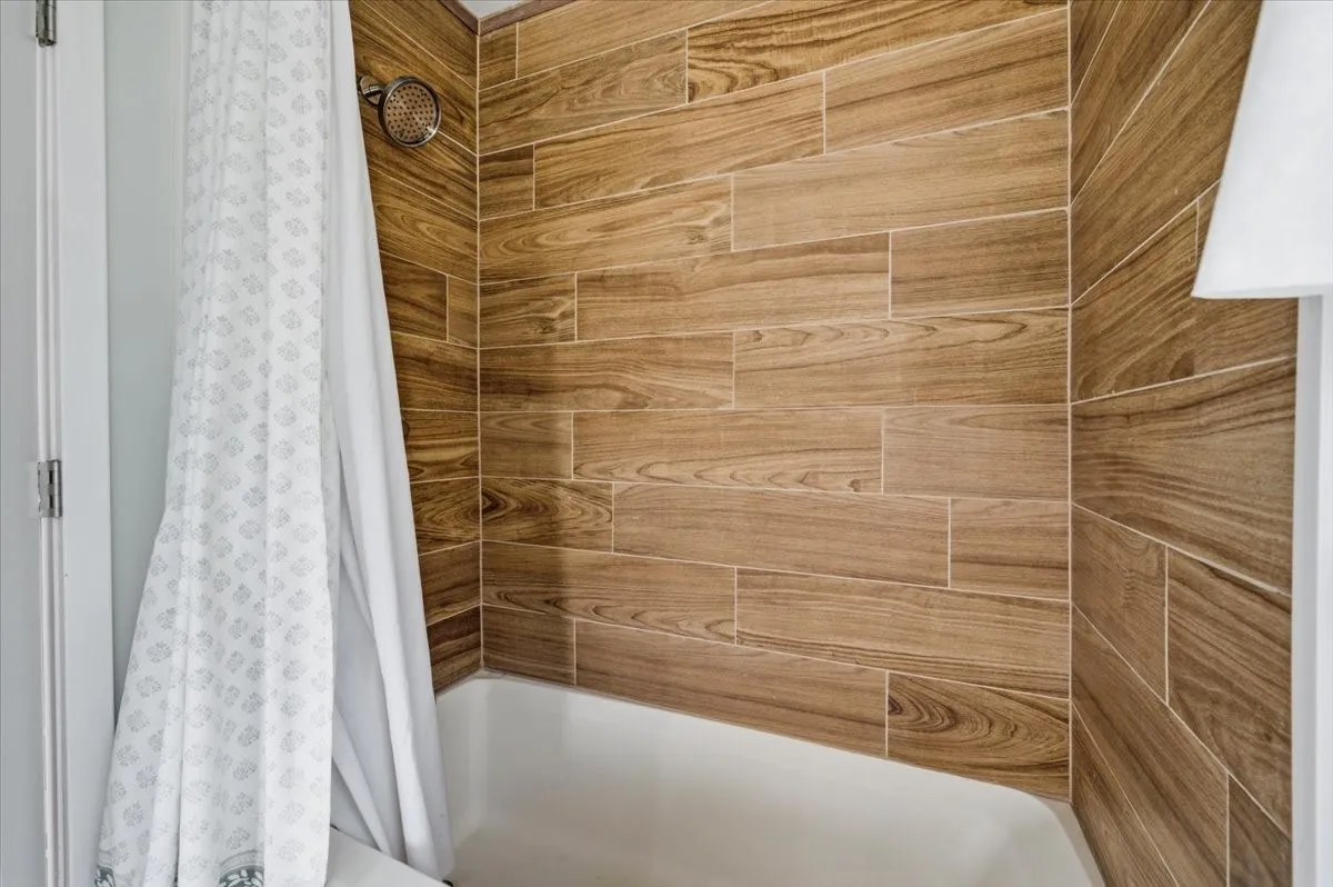 Bathtub featuring wood-finish wall tiling and a polished chrome showerhead