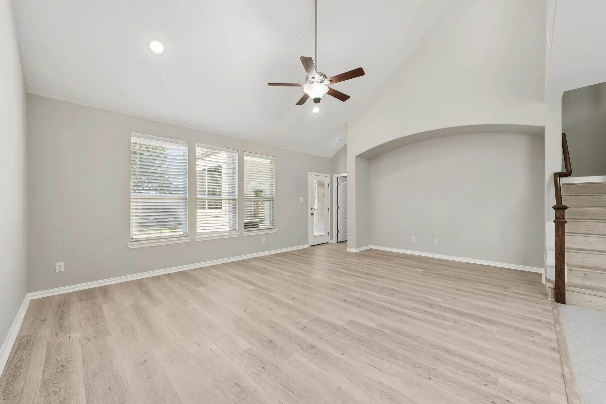 Living room with high vaulted ceiling, stairway ceiling fan, and recessed lighting