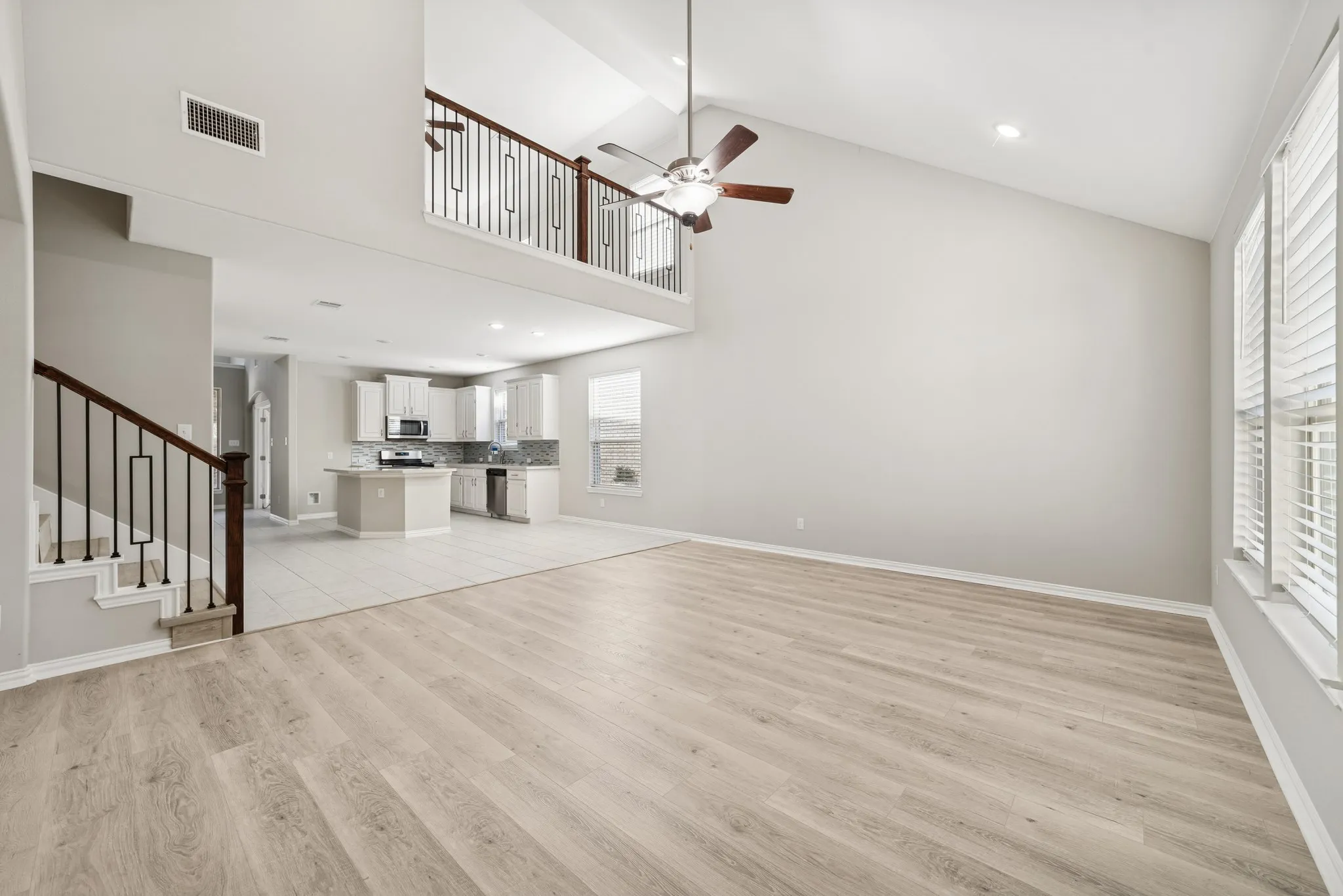 Huge living room with healthy amount of natural light, high vaulted ceiling, ceiling fan, and stairs