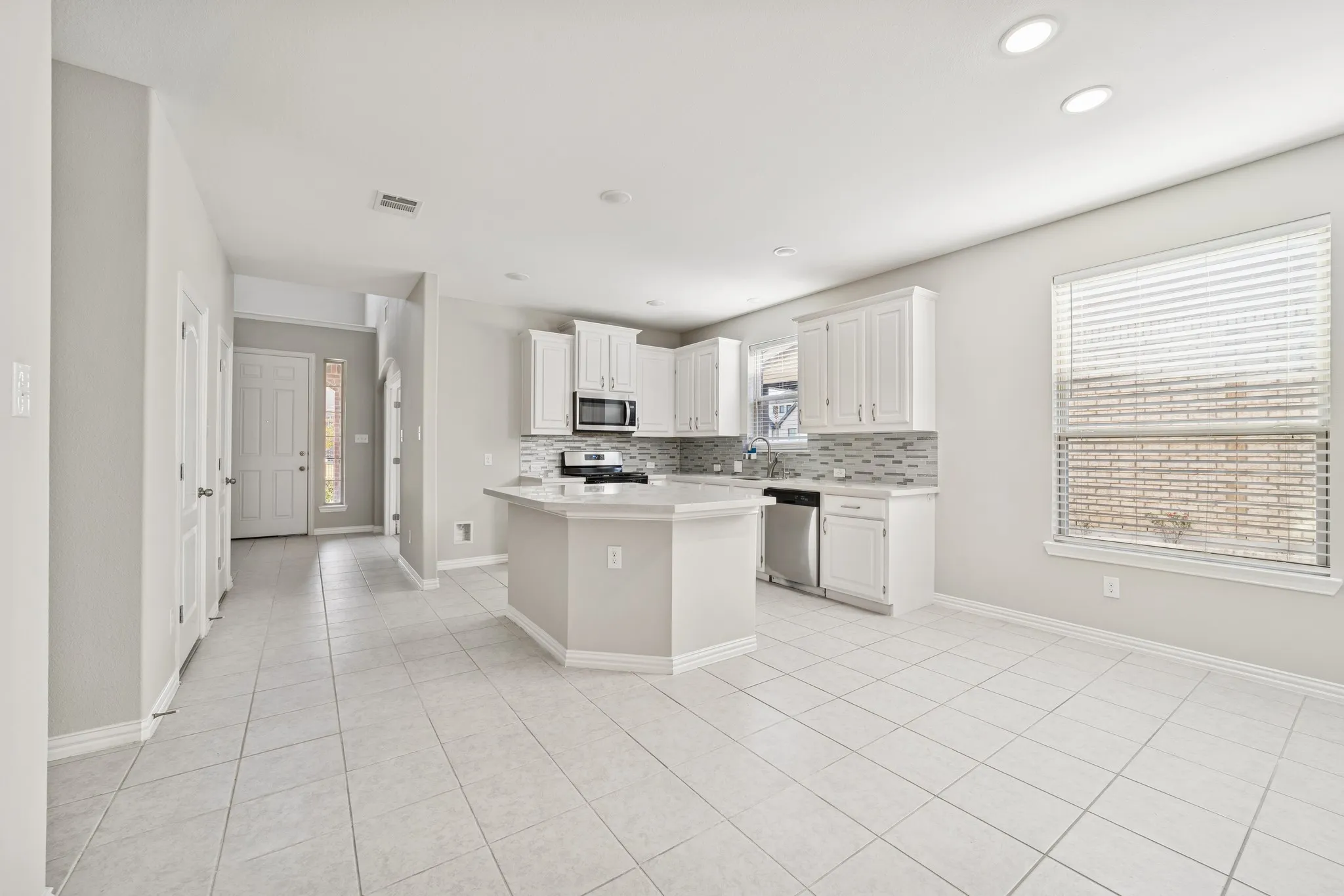 Kitchen with light tile patterned flooring, a kitchen island, tasteful backsplash, white cabinetry, and recessed lighting