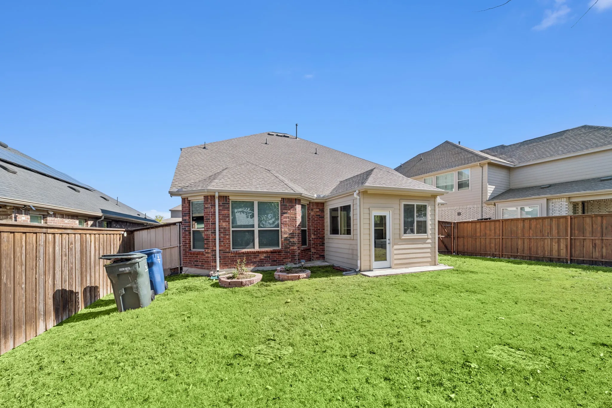 Back of property featuring a fenced backyard, a shingled roof, and brick siding