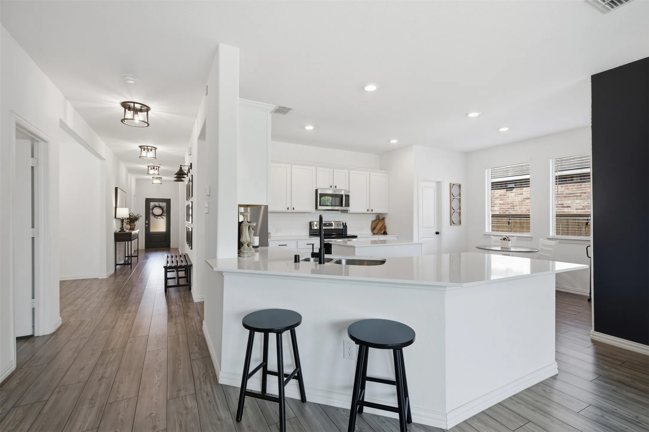 Open kitchen with crisp white cabinets topped with crown molding stainless steel appliances and black hardware continue the classic back and white theme