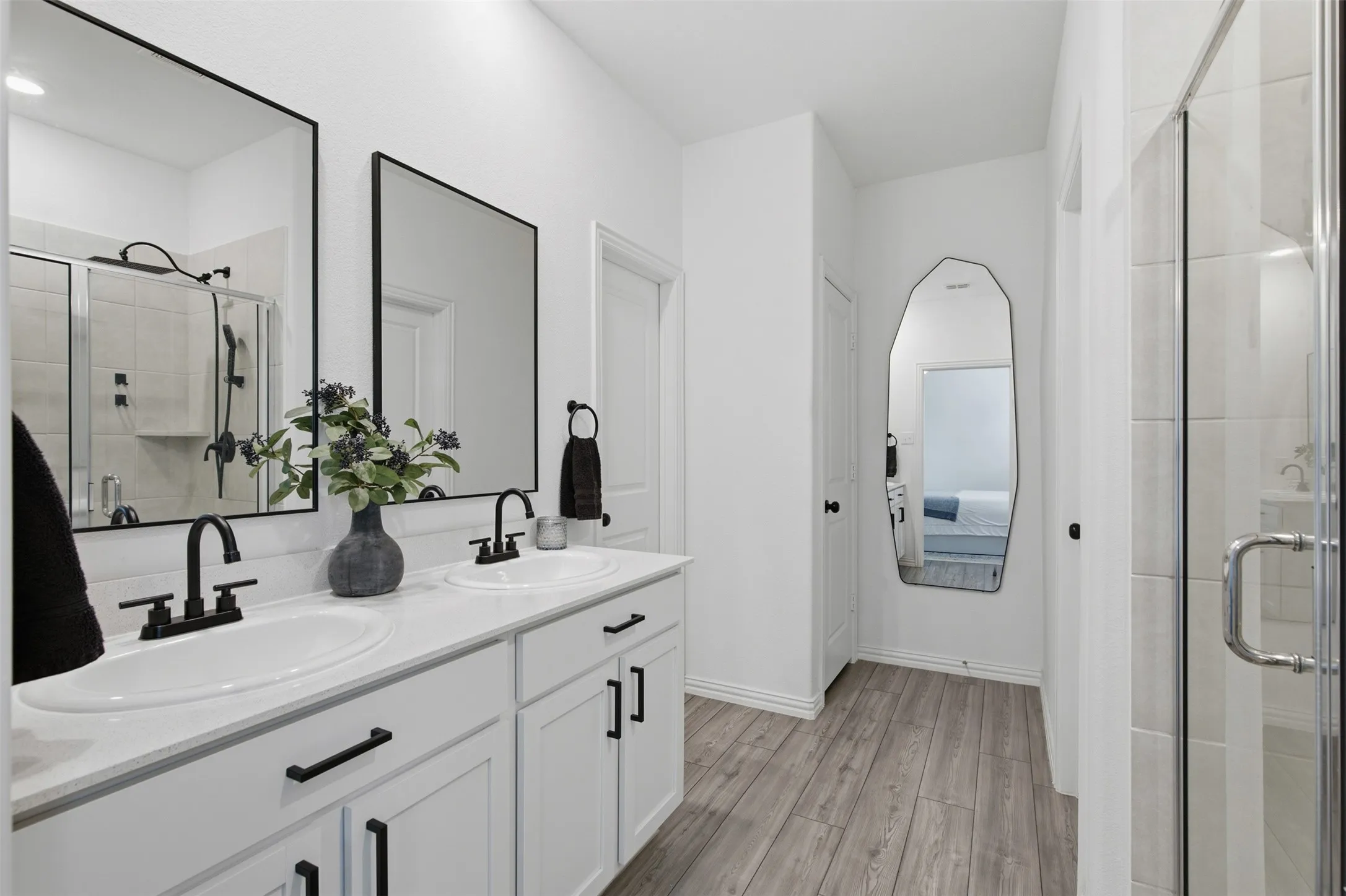 Main bath with large walk-in shower, dual vanity with framed black mirrors, black hardware and plumbing fixtures. Walk-in closet and linen closet located inside the bath