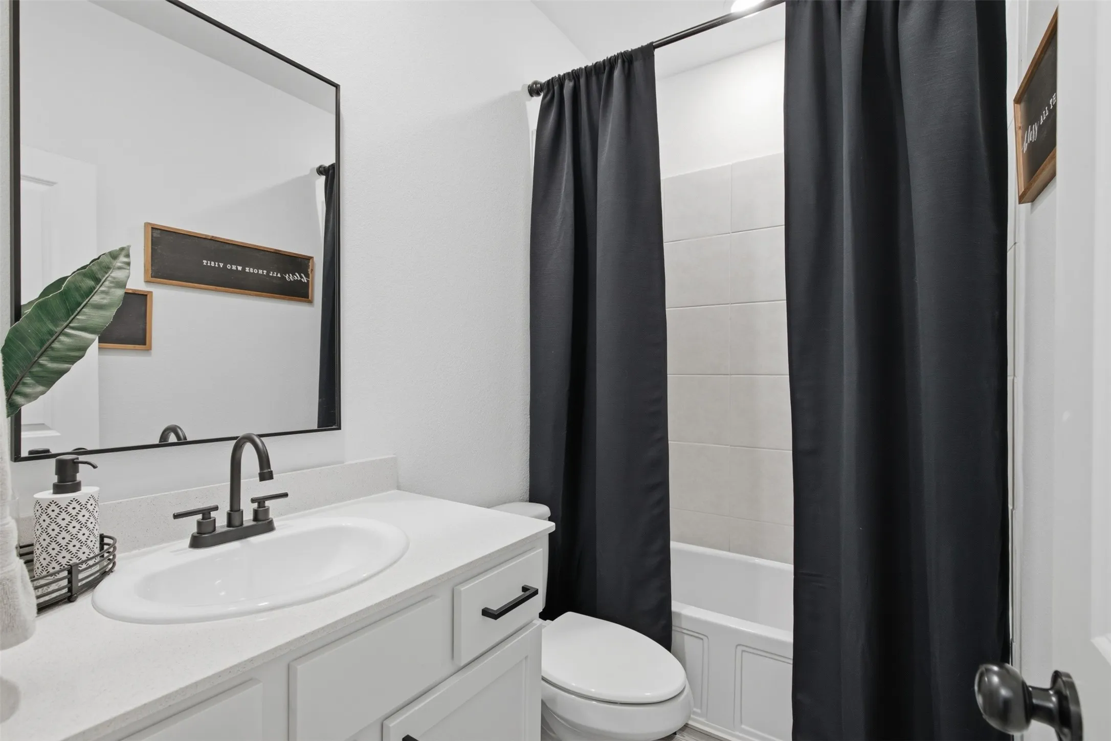 Main full bath, with tile surround in tub/shower combo, black framed mirror, matching black hardware & plumbing fixutres