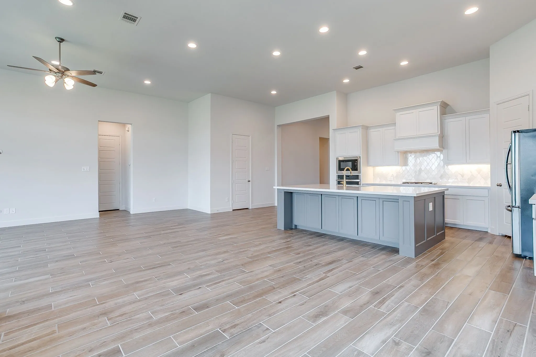 Spacious kitchen featuring a large island with gray cabinetry, white countertops, and a full suite of stainless steel appliances