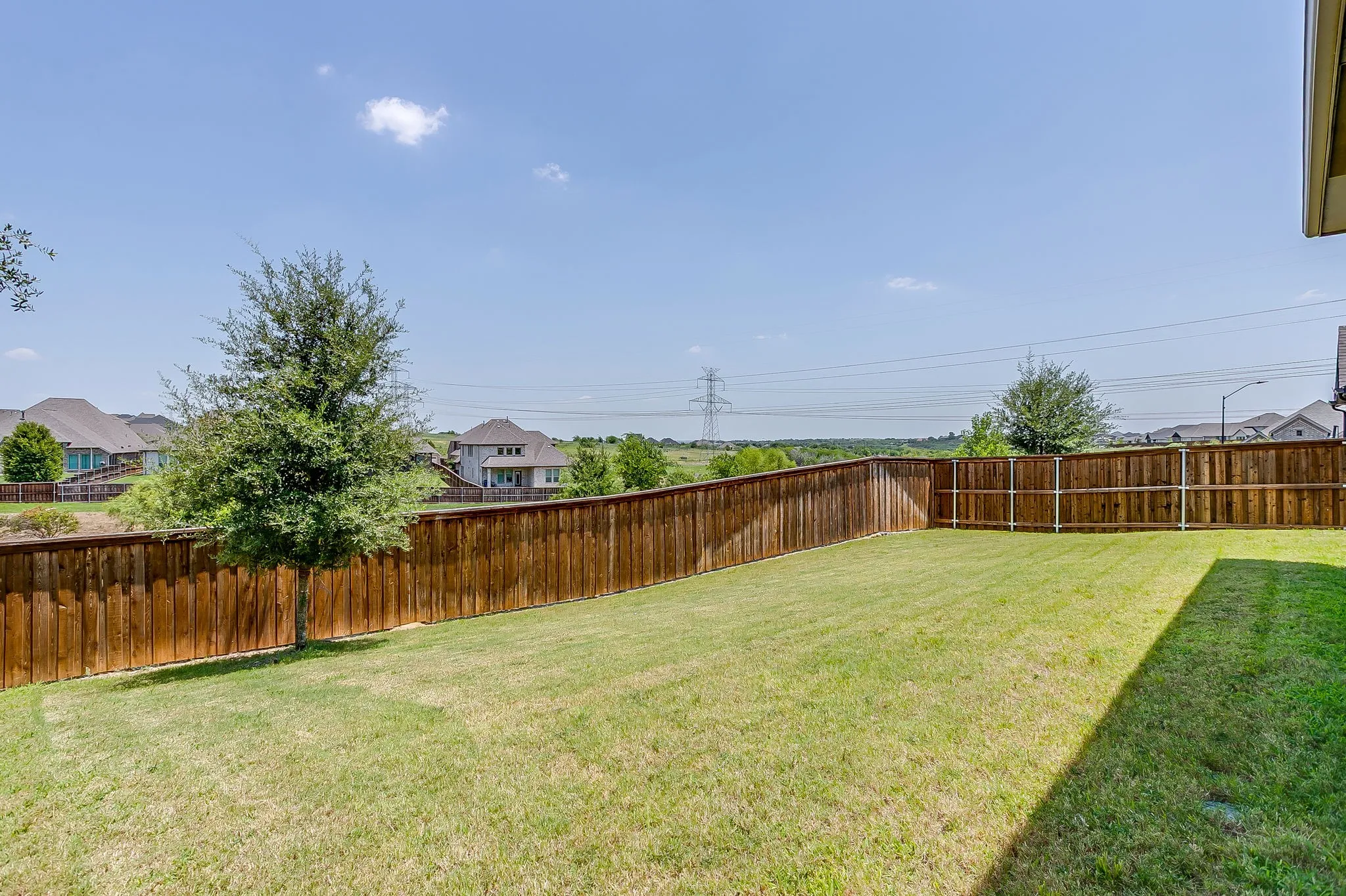 Expansive backyard featuring a natural wood privacy fence, a verdant lawn, and a mature tree