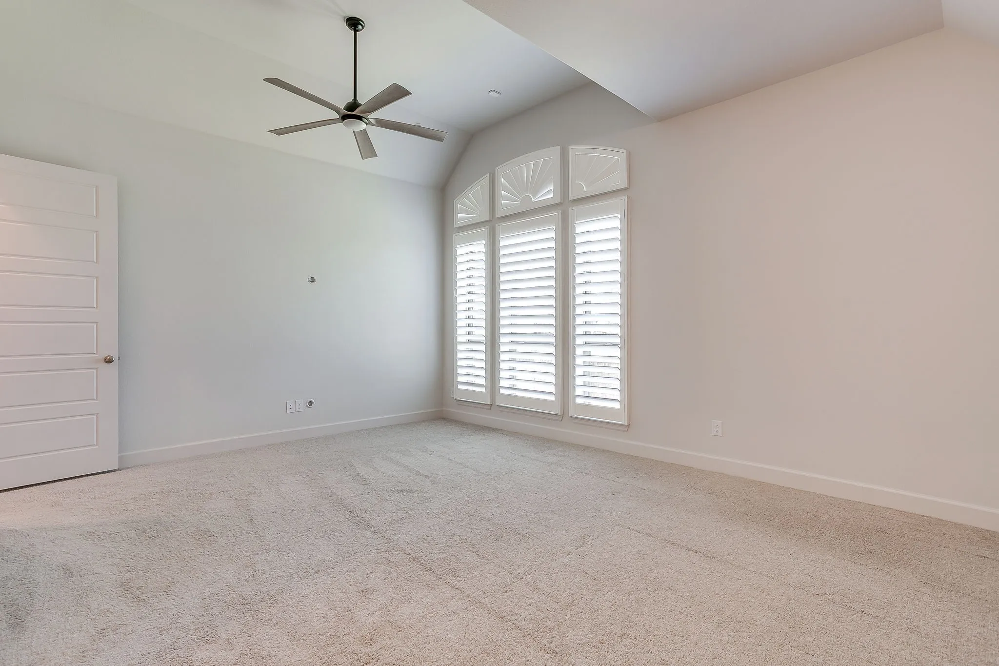Carpeted room featuring a ceiling fan, vaulted ceiling, and an arched window with plantation shutters