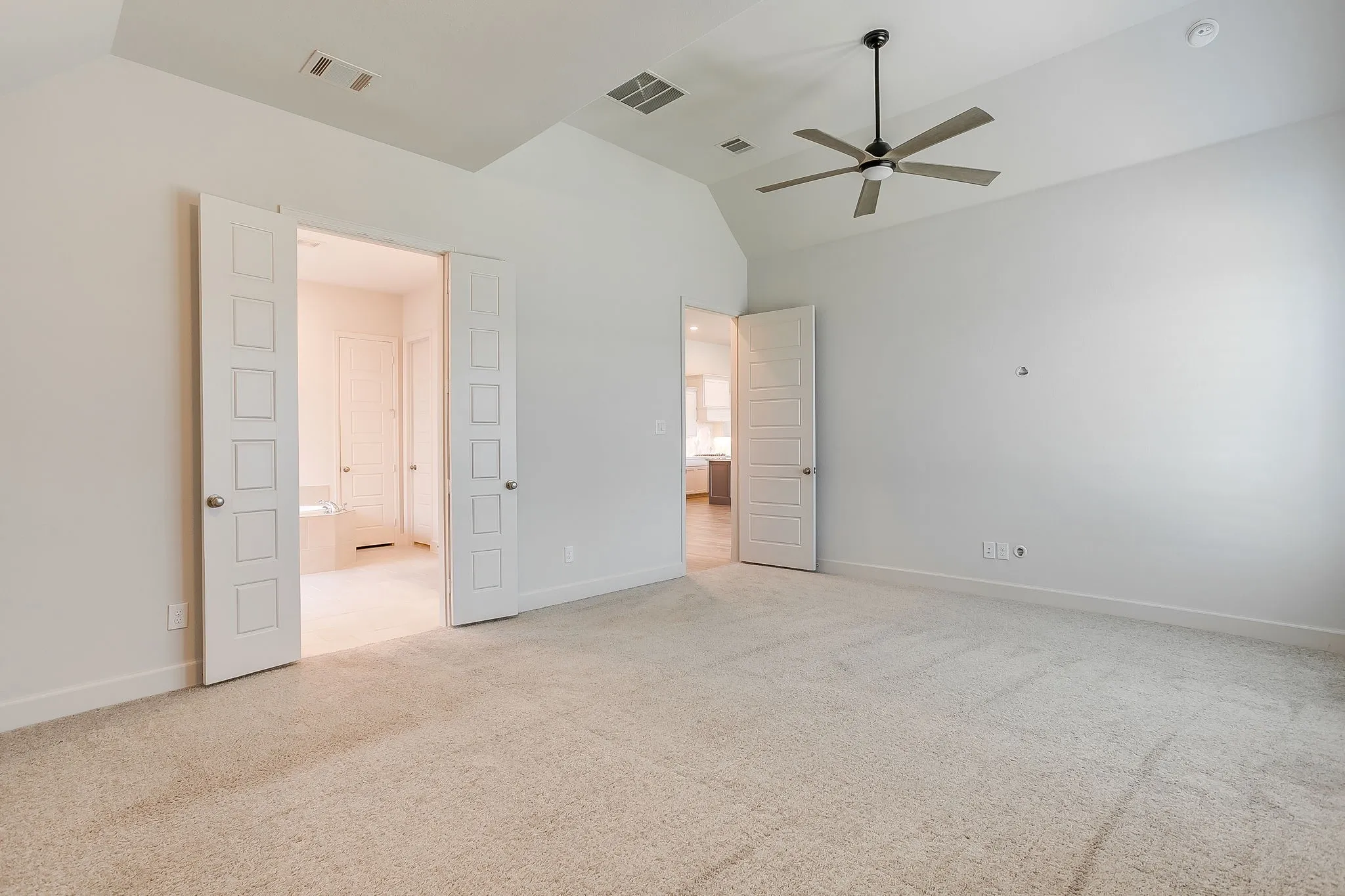 Carpeted room featuring a vaulted ceiling with a ceiling fan, dual panel doors, and a single panel door leading to separate areas