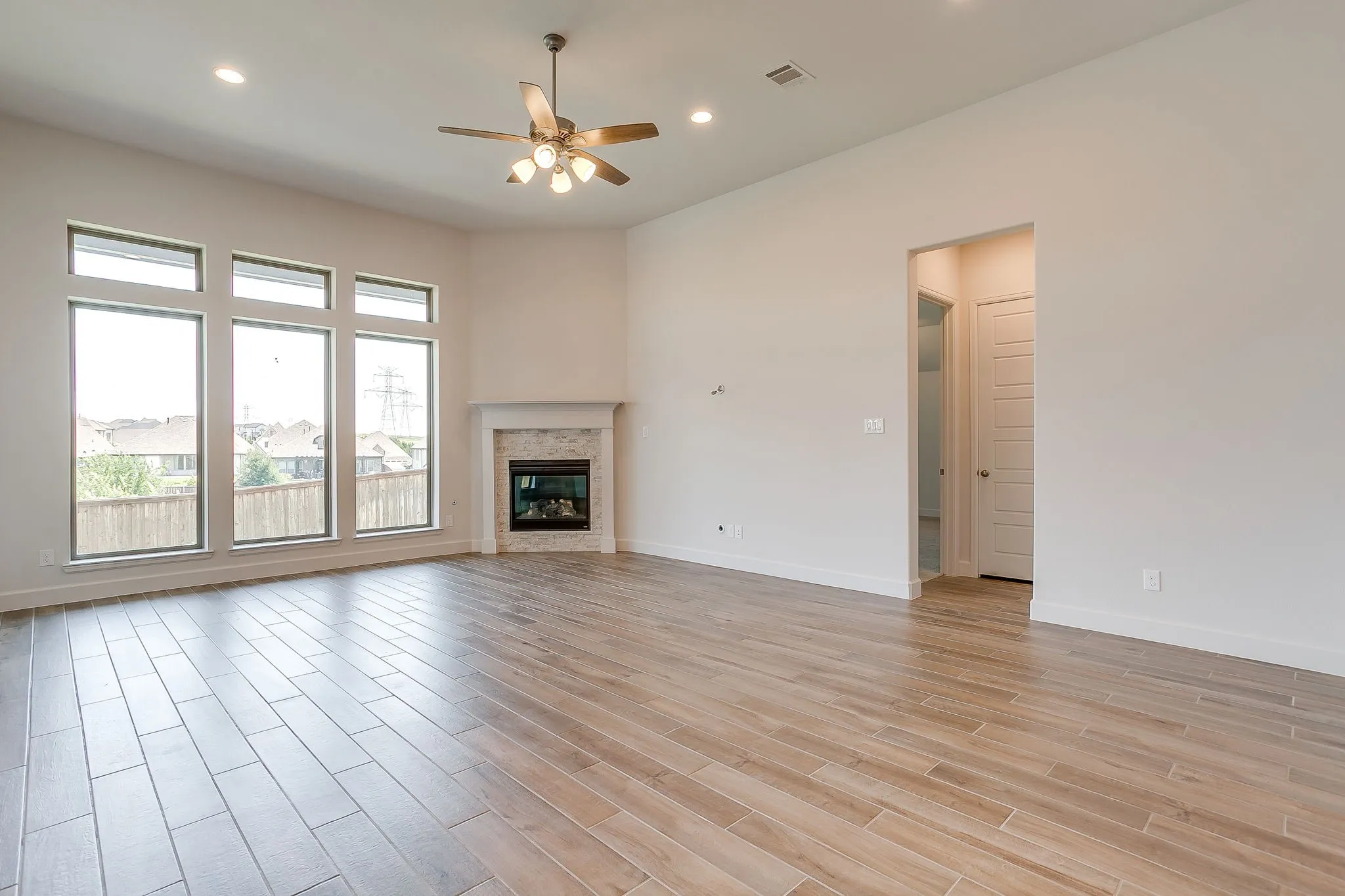 Open-concept living space featuring wood-finish flooring, a contemporary fireplace with a stone surround, and a ceiling fan with integrated lighting