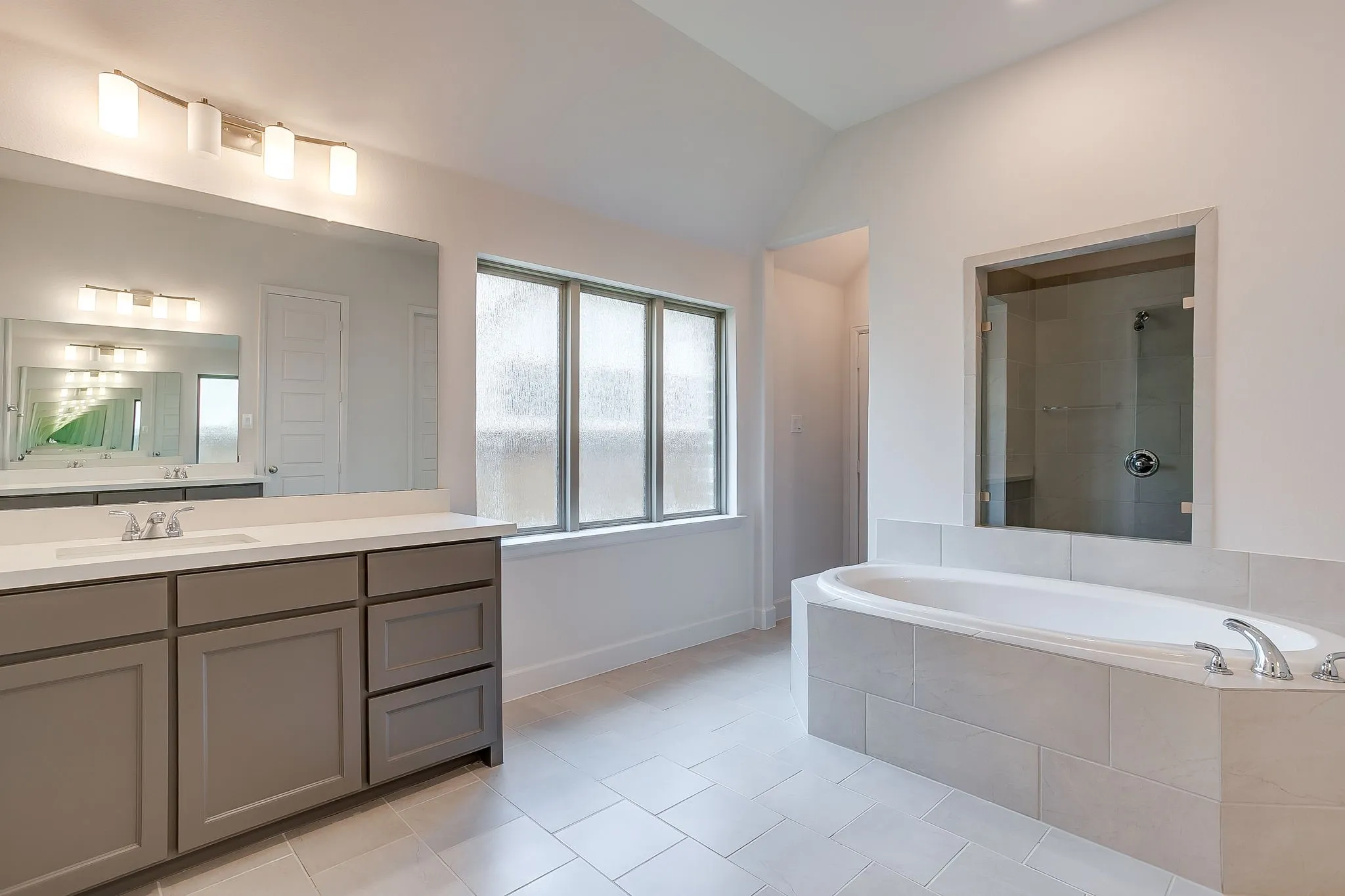 Spacious bathroom featuring a built-in soaking tub, glass-enclosed shower, dual vanity with shaker-style cabinetry, large mirror, and frosted windows