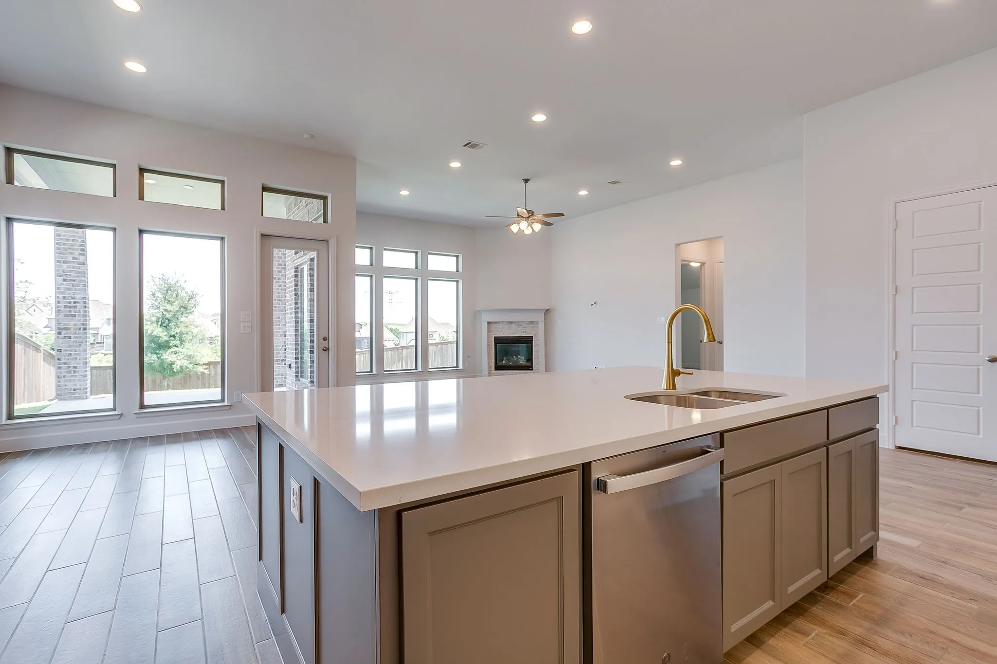 Kitchen island featuring a double basin sink with a gold-tone faucet, a built-in stainless steel dishwasher, and cabinetry with paneled fronts